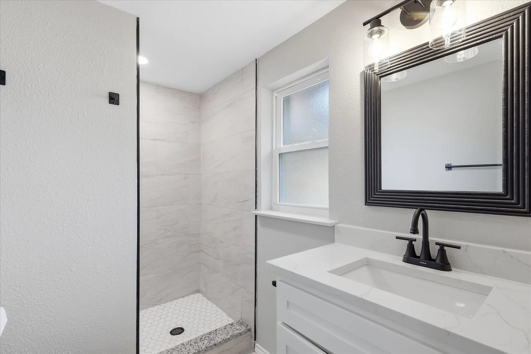 Contemporary bathroom featuring a white vanity with an integrated sink, a dark framed mirror, and a three-light fixture