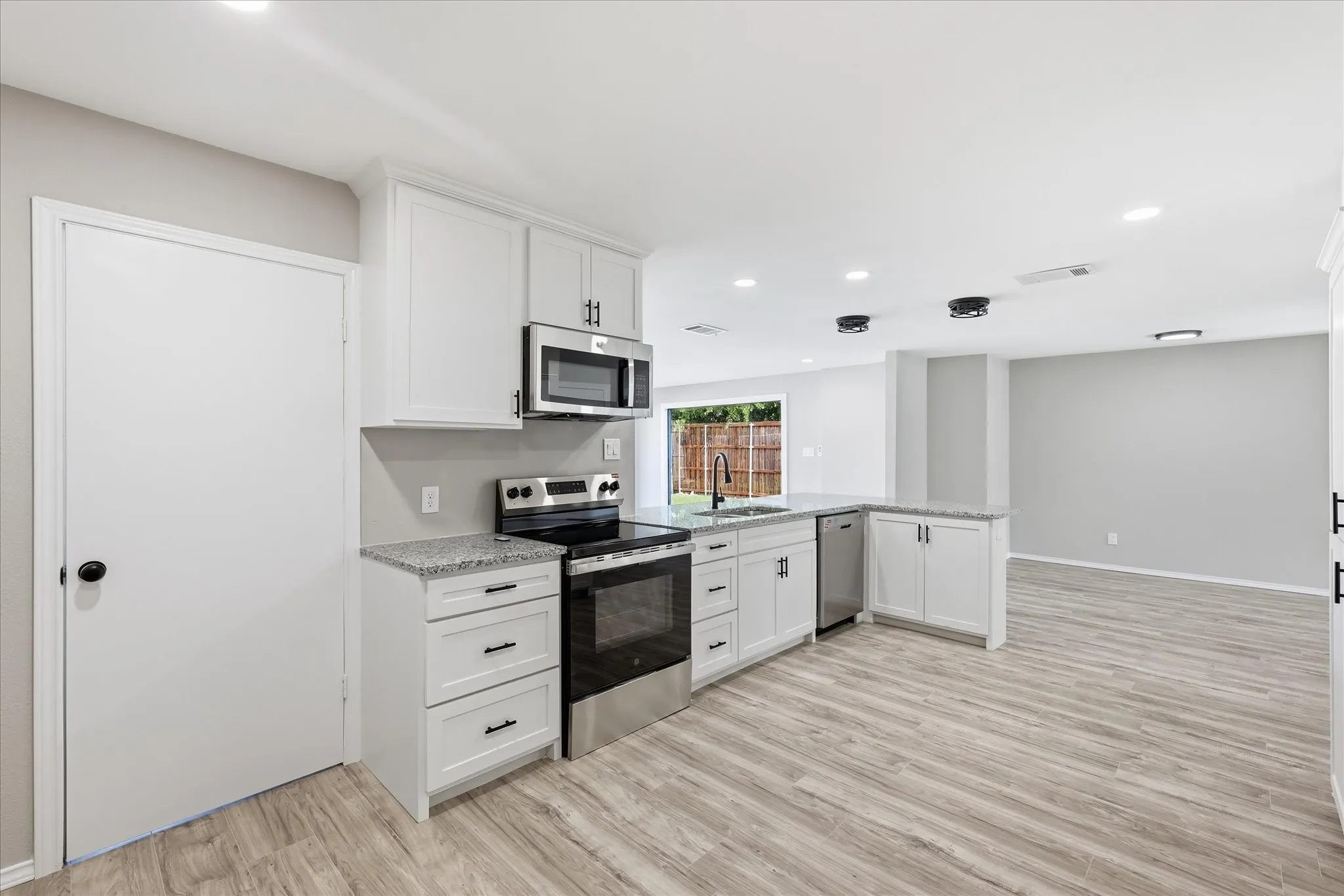 Kitchen featuring white cabinetry, granite-style countertops, stainless steel appliances, and wood-finish flooring