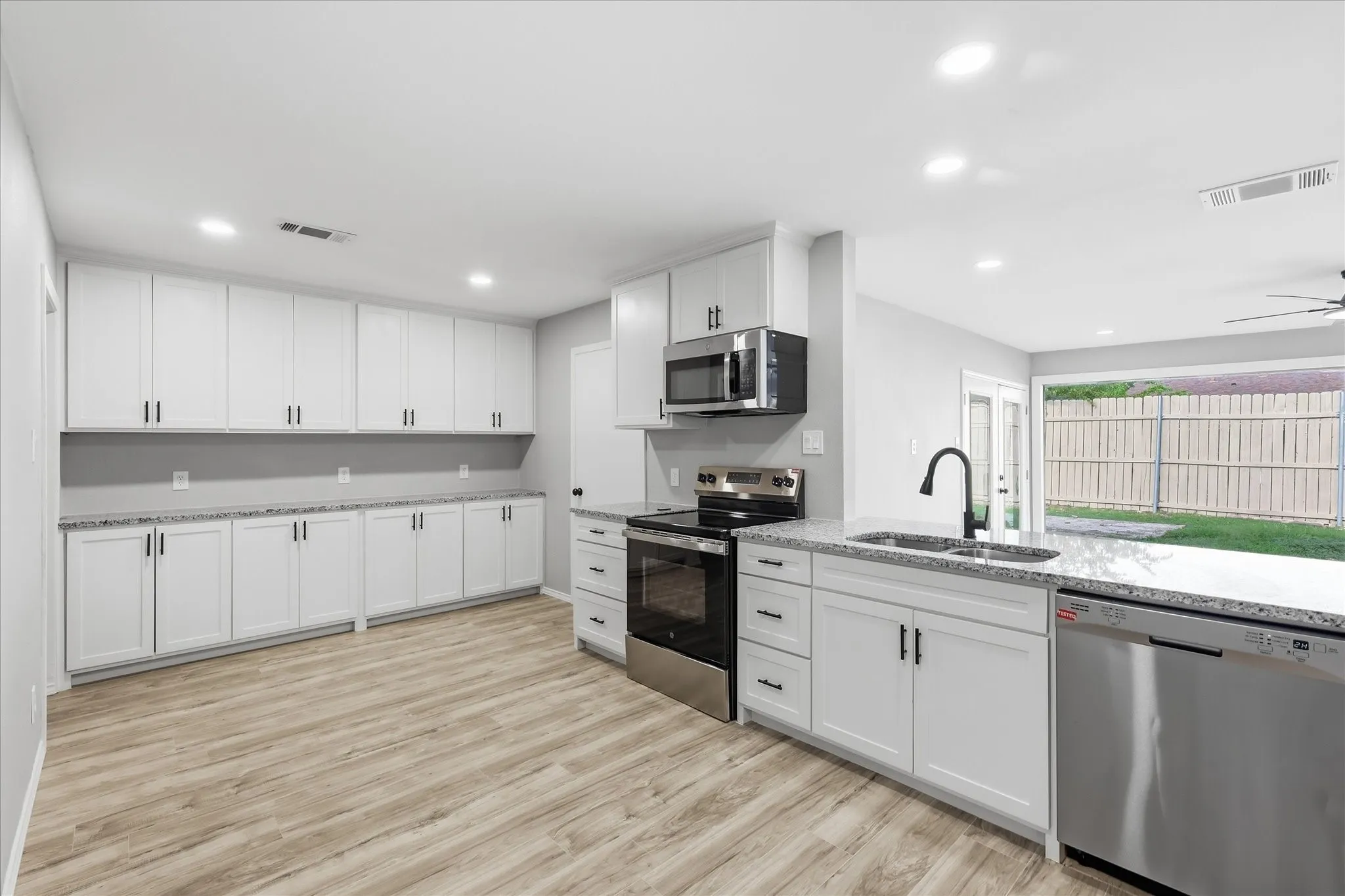 Contemporary kitchen featuring white cabinetry, light-toned wood-finish flooring, recessed lighting, stainless steel appliances, and granite-style countertops