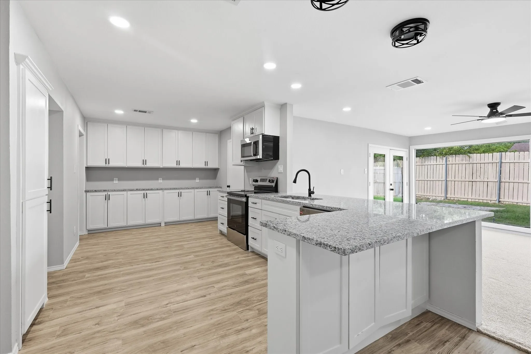 Expansive kitchen featuring white shaker cabinetry, light-toned wood-finish flooring, and a large island with a speckled countertop and integrated sink