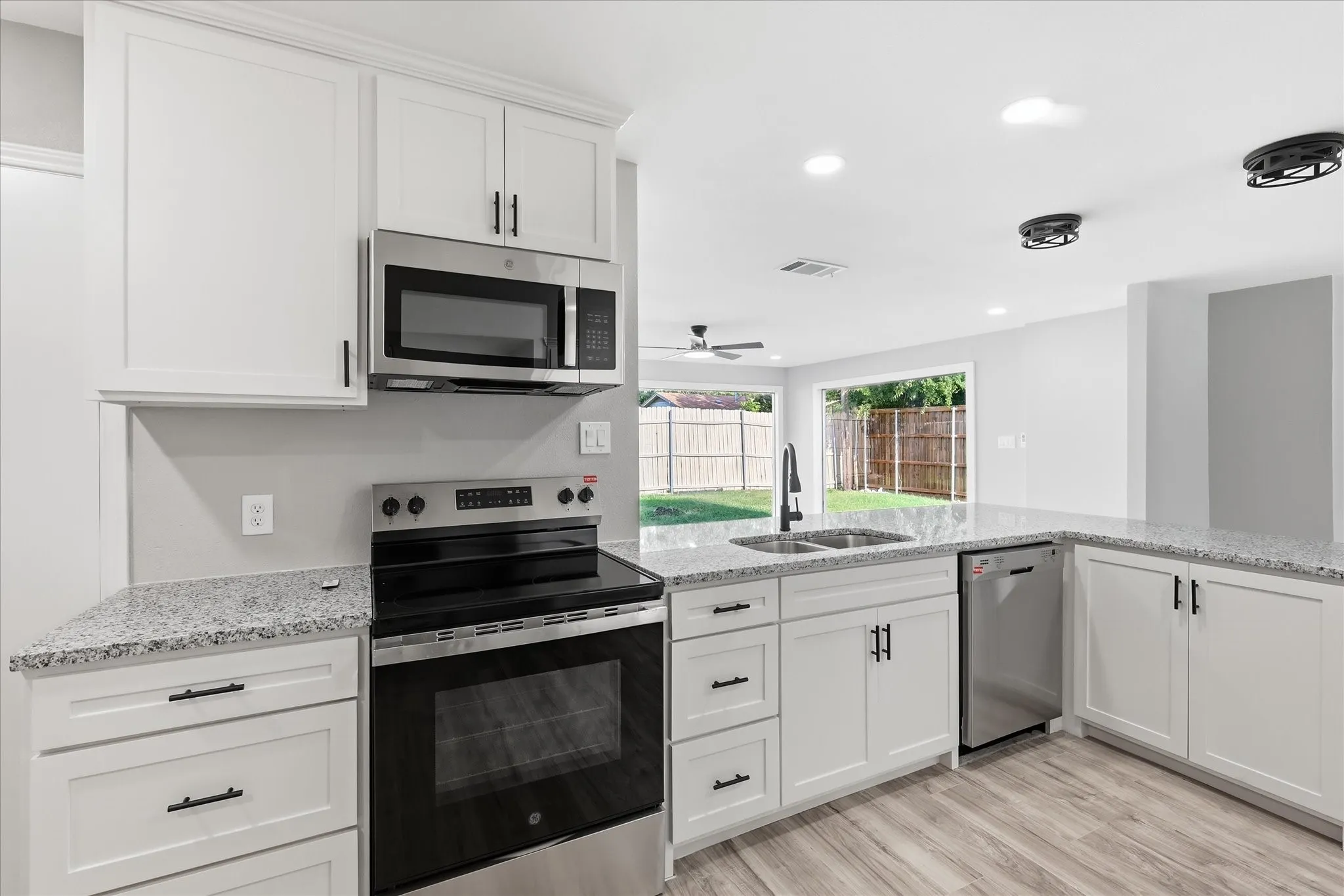 Modern kitchen featuring white shaker cabinetry, stainless steel appliances, speckled countertops, wood-finish flooring, and recessed lighting