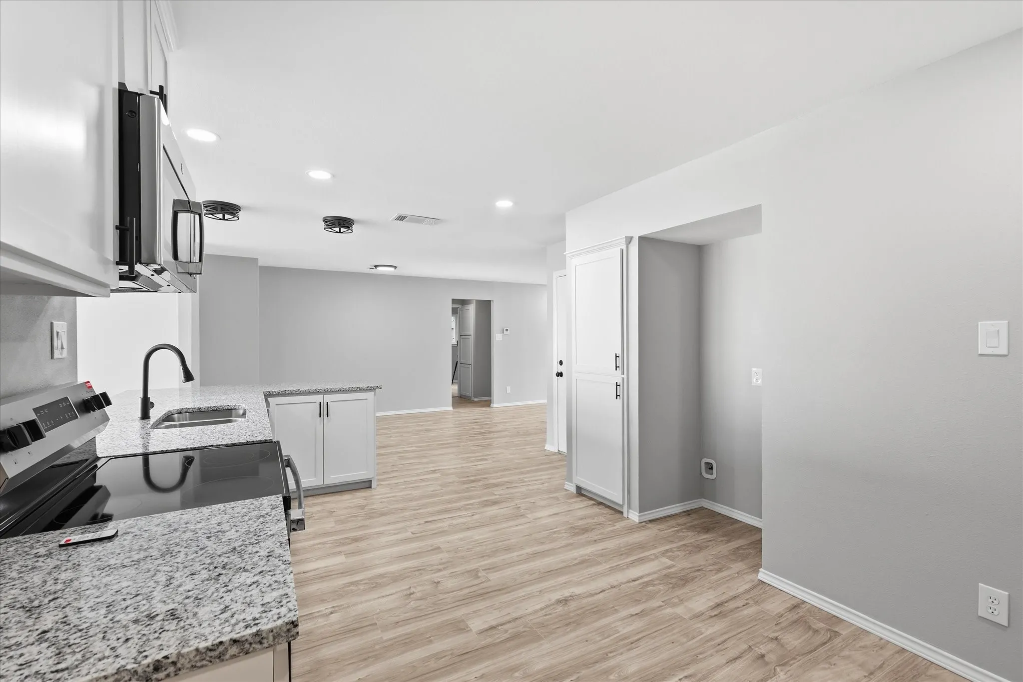 Open-concept kitchen featuring granite countertops, white cabinetry, a black range, and wood-finish flooring