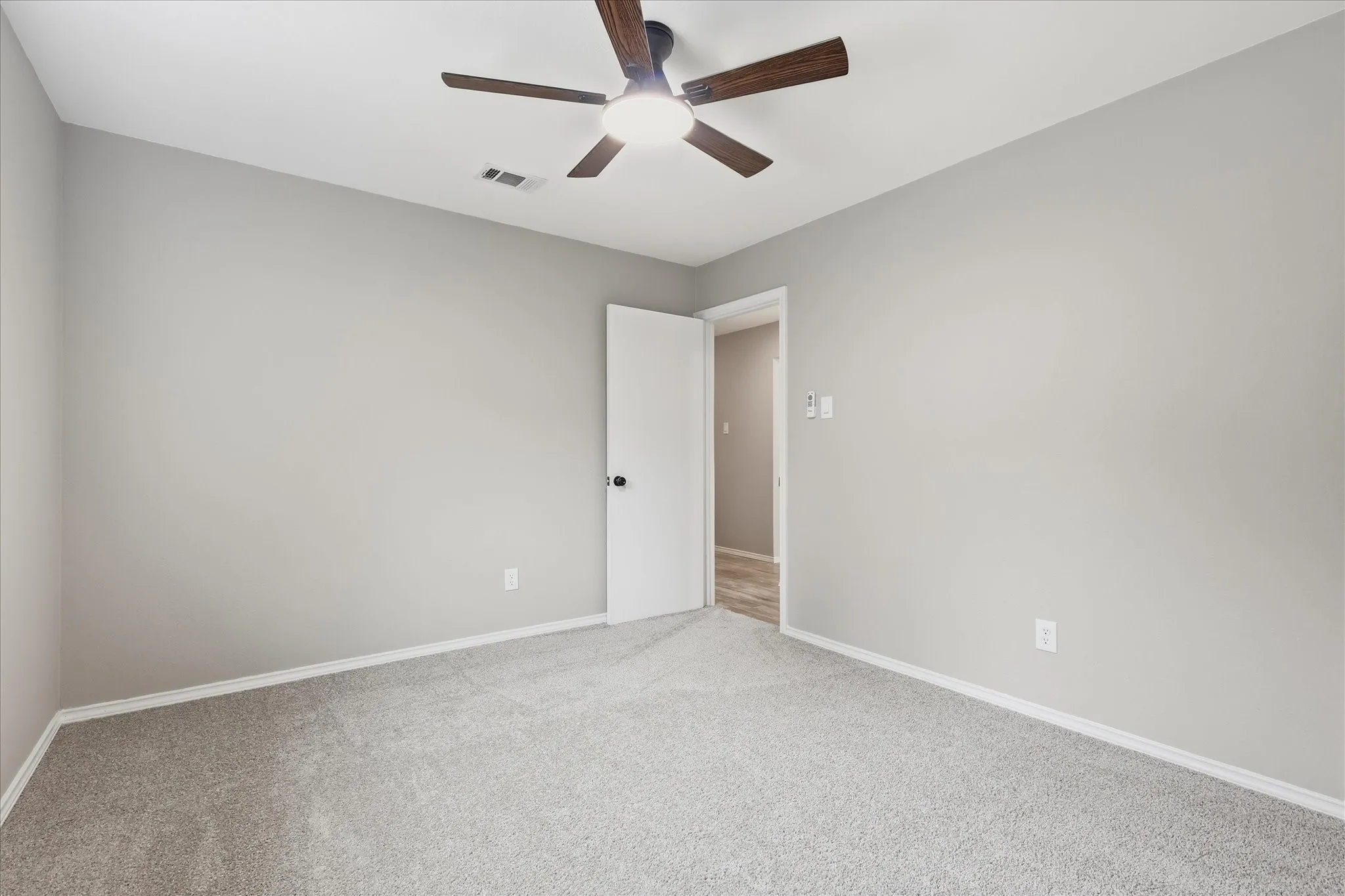 Spacious room featuring light gray wall paint, gray carpeting, white baseboards, and a ceiling fan with integrated lighting