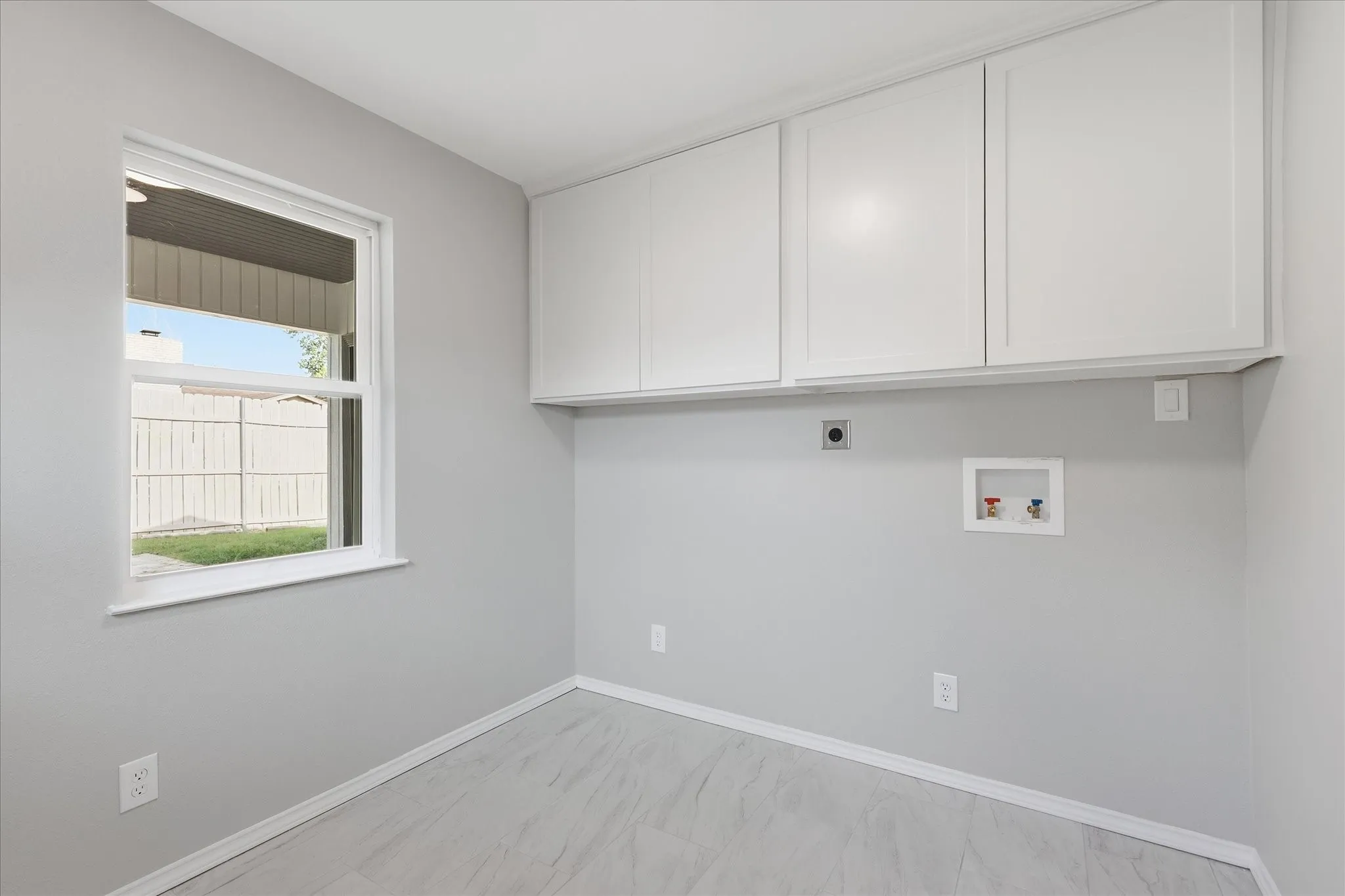 Laundry area featuring overhead white cabinetry, a single window, and light-toned wood-finish flooring