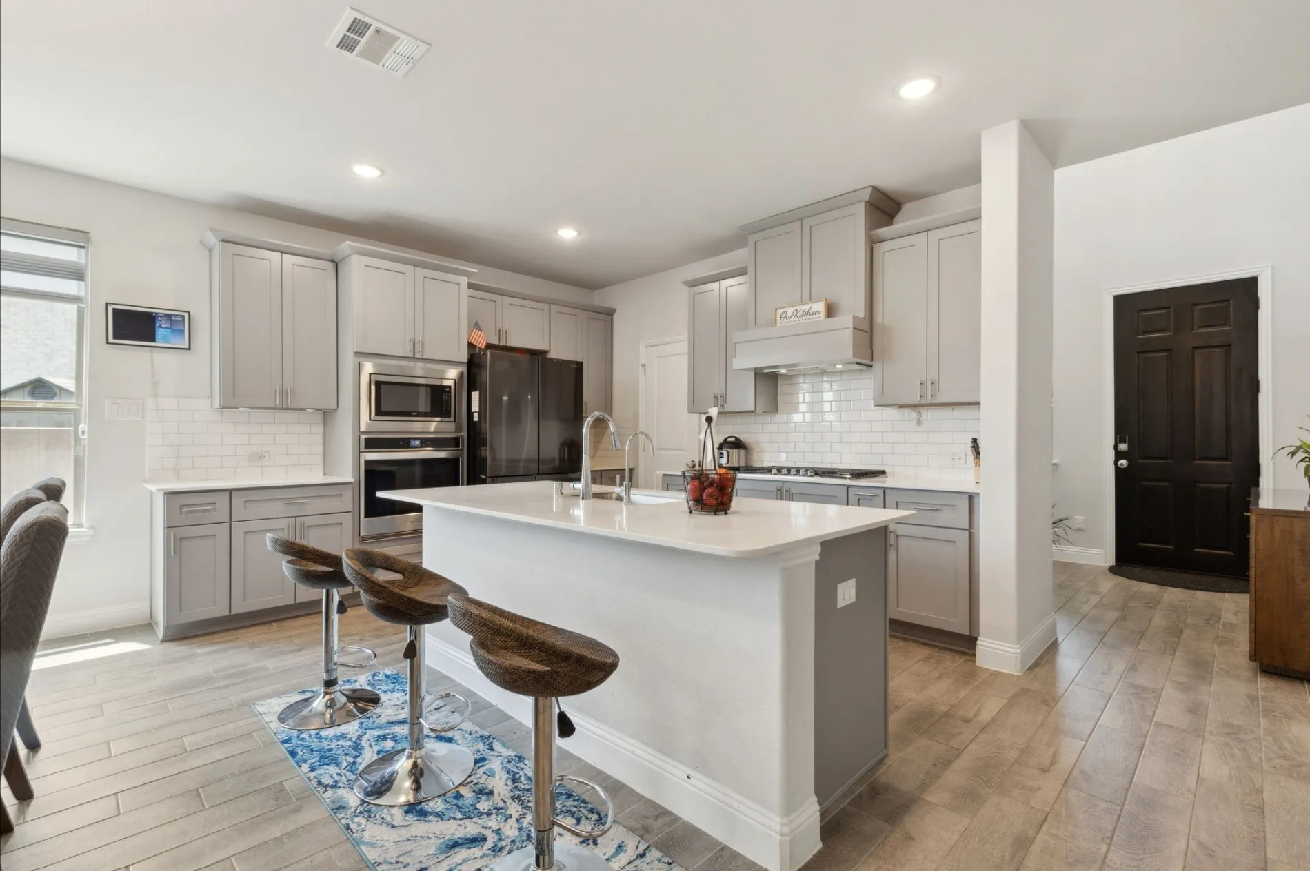 Kitchen featuring an expansive center island with seating, light gray cabinetry, built-in stainless steel appliances, a subway tile backsplash, and light wood-finish flooring