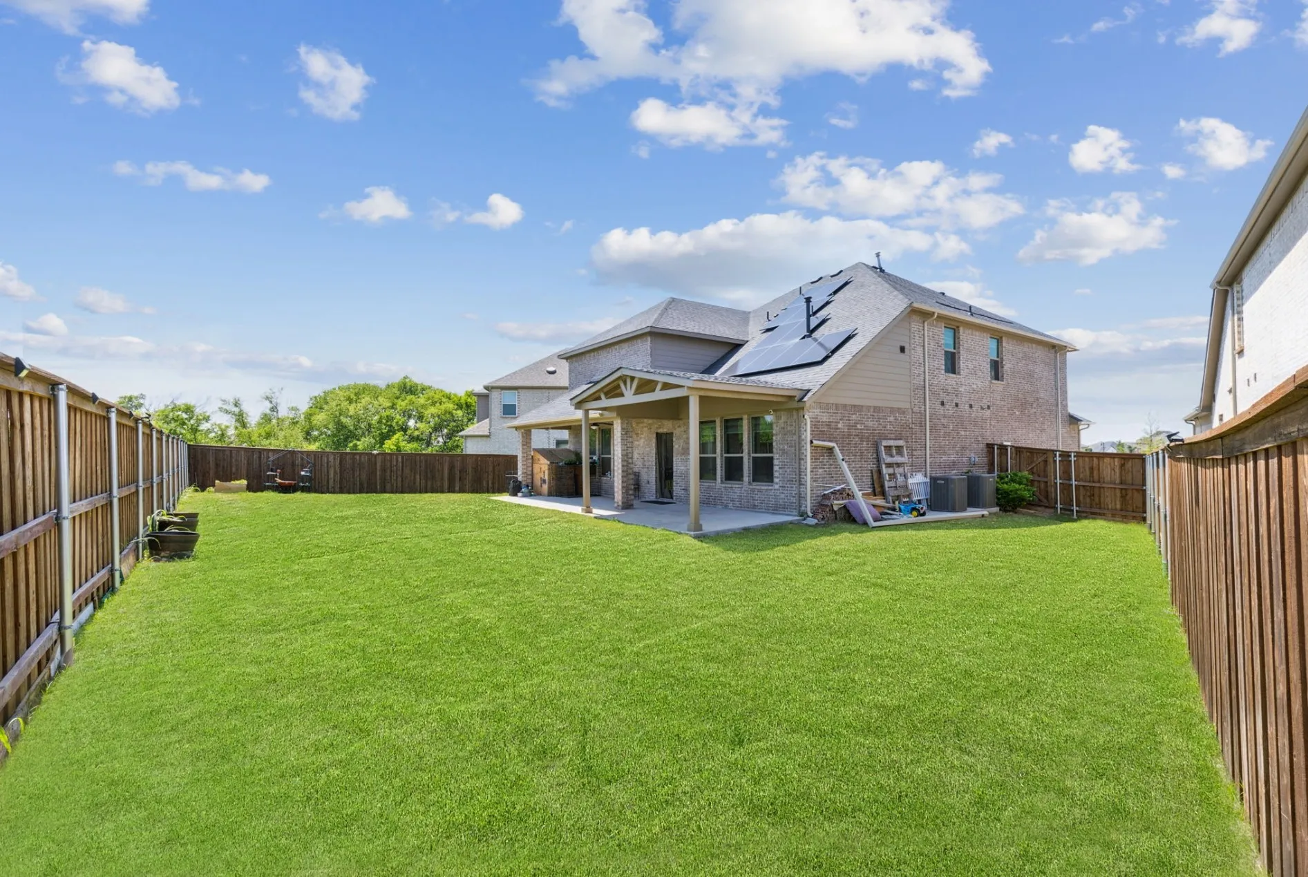 Expansive backyard featuring a lush lawn, privacy fencing, and a covered patio