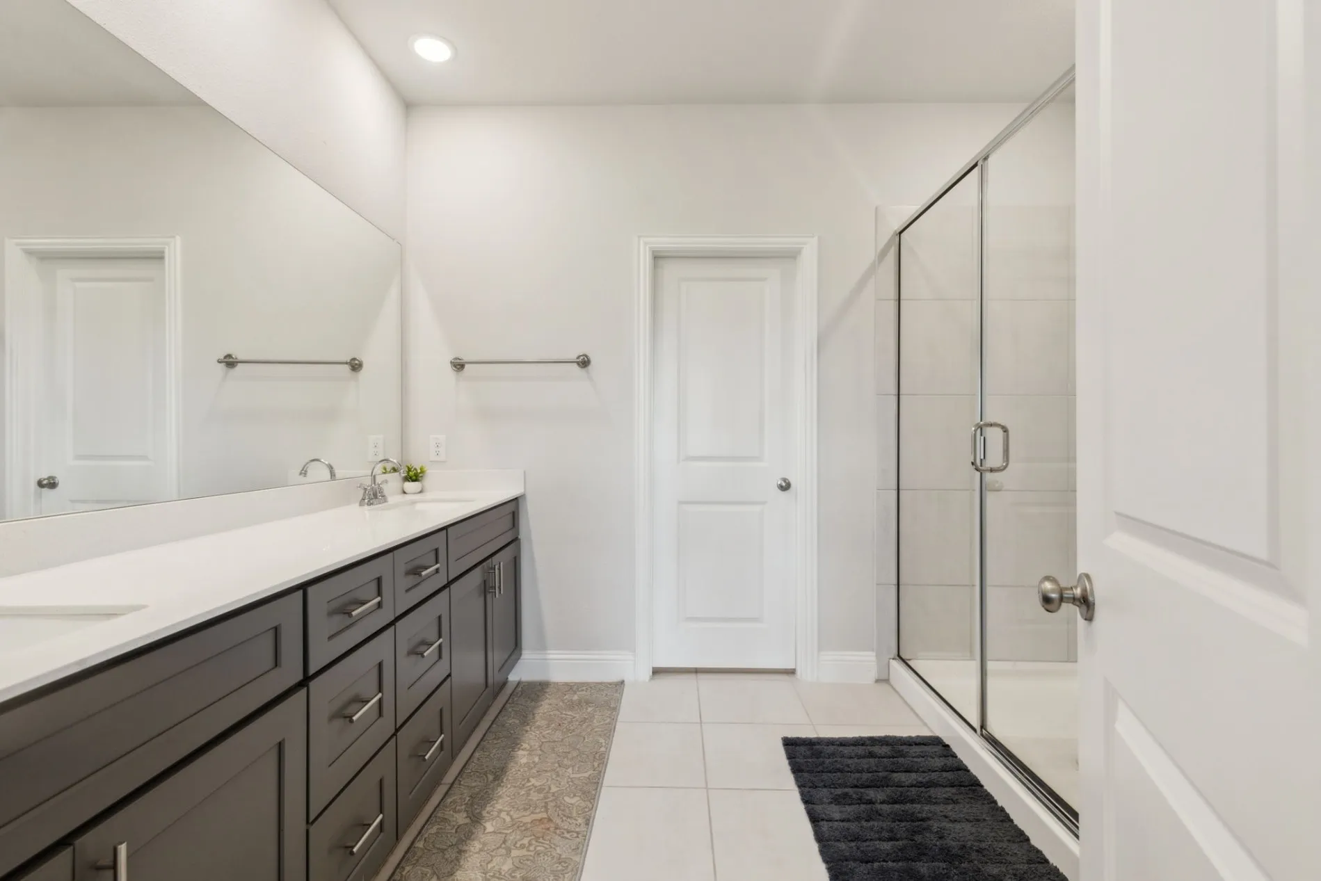 Bathroom featuring a dual vanity with dark wood cabinetry and a light-toned countertop, a frameless glass shower enclosure with white tile surround, and recessed lighting