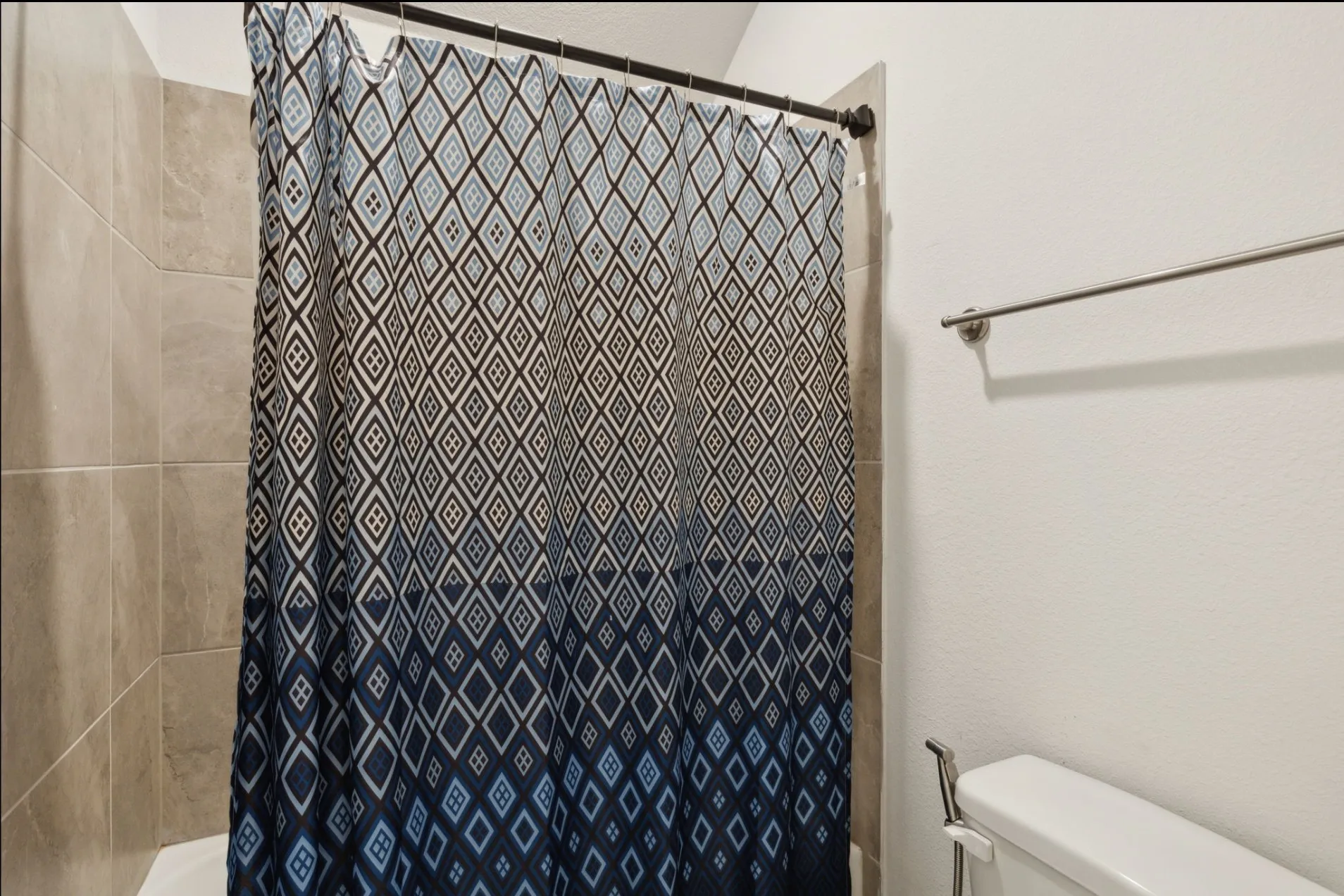 Tiled shower surround with a dark rod, a white toilet, and a wall-mounted towel bar