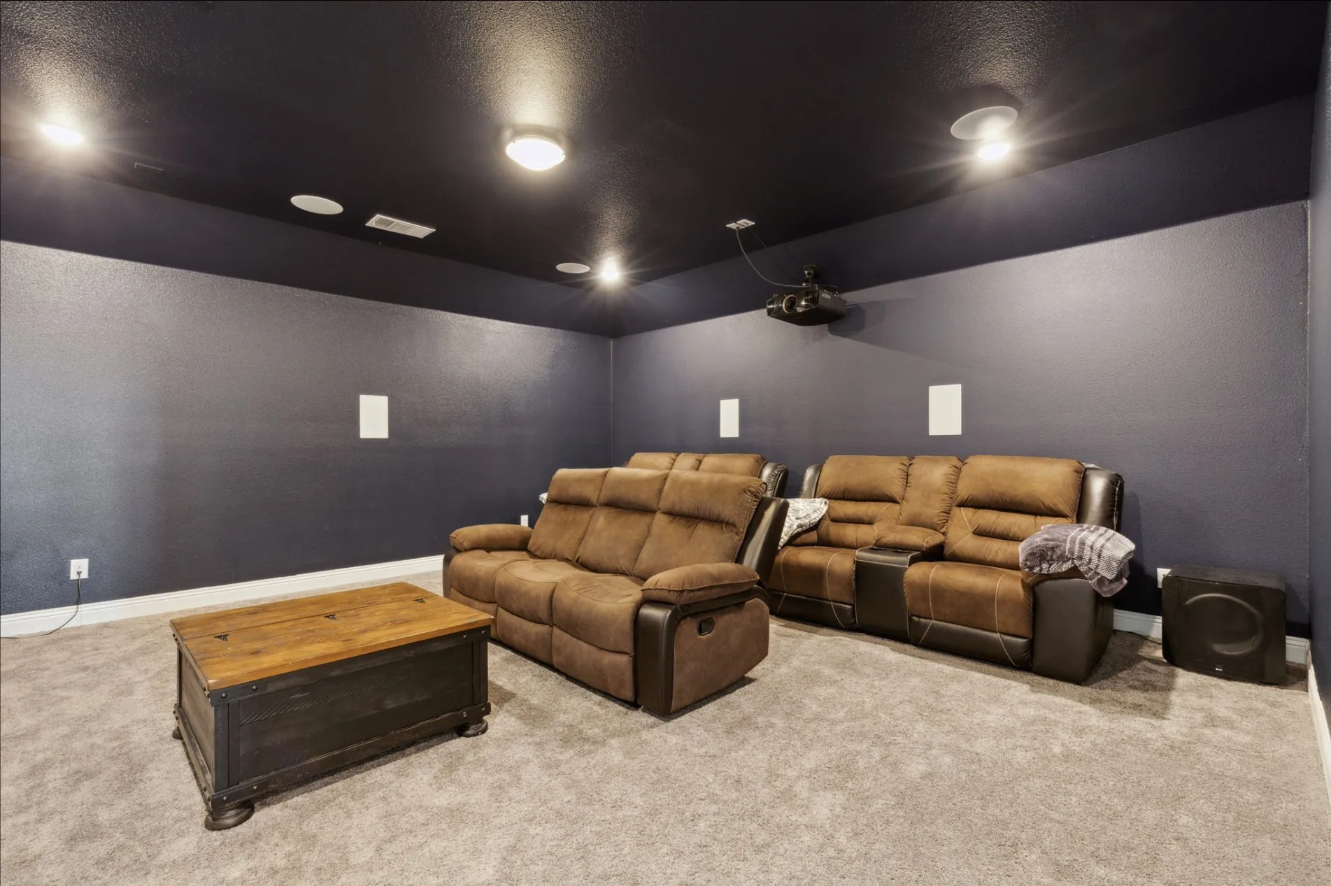 Dedicated media room with dark walls and ceiling, wall-mounted speakers, and recessed lighting