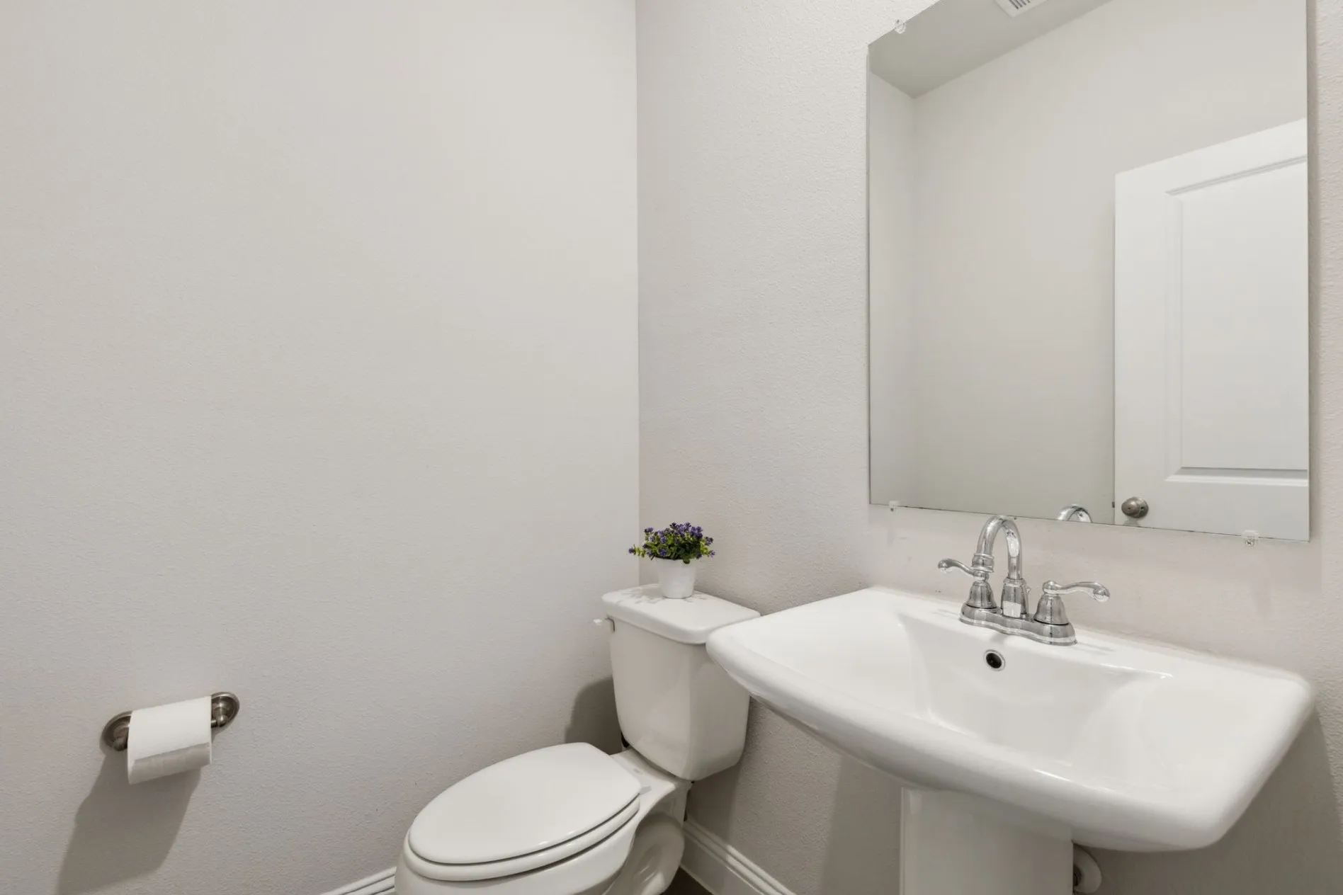 Brightly lit powder room featuring a pedestal sink, wall-mounted mirror, and white toilet