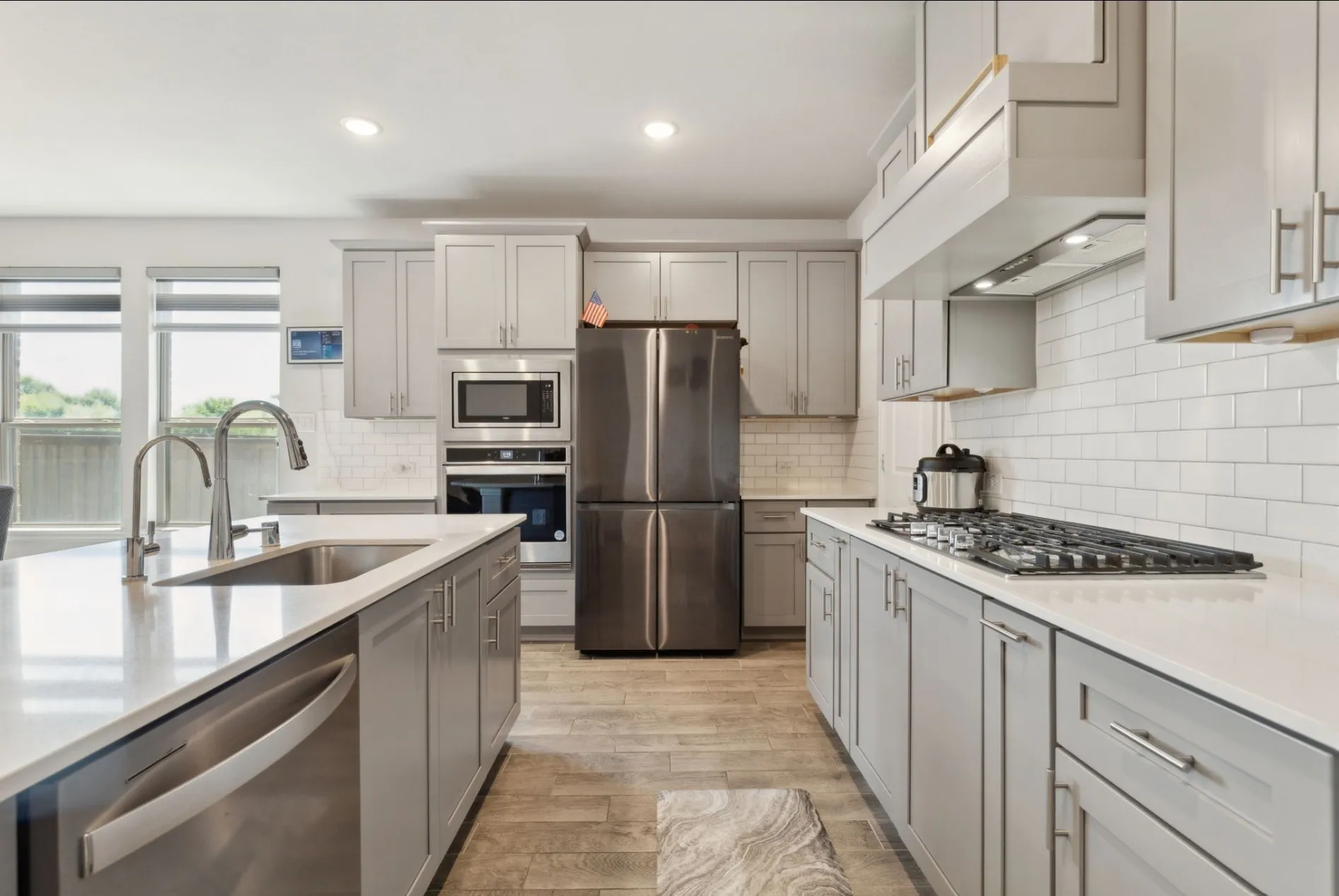 Modern kitchen featuring light gray cabinetry, stainless steel appliances, white subway tile backsplash, and wood-finish flooring