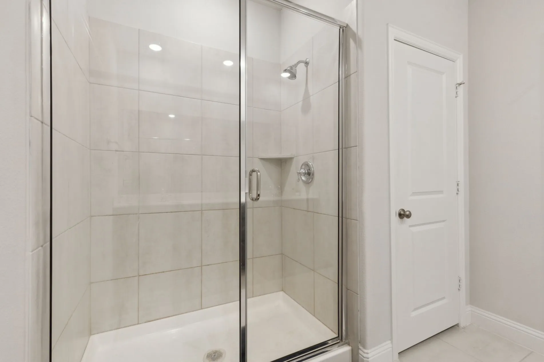 Walk-in shower featuring clear glass enclosure, neutral tile surround, built-in shelving, and polished chrome fixtures