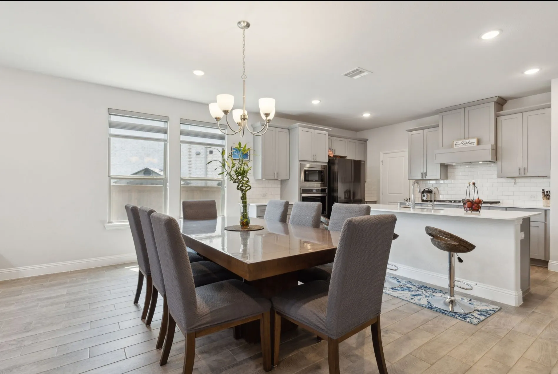 Open-concept dining area featuring wood-finish flooring, a contemporary chandelier, and a bright kitchen beyond