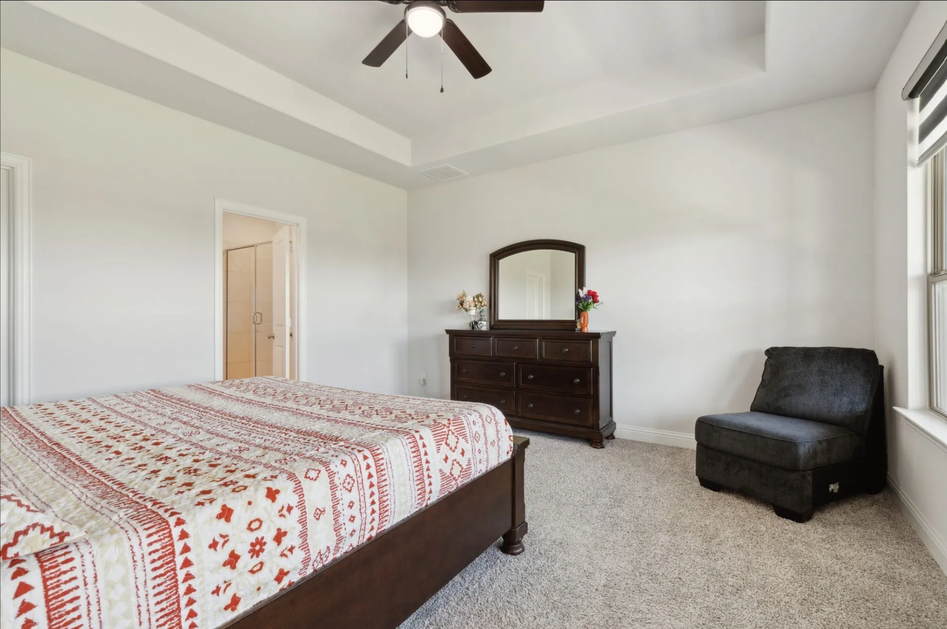 Carpeted bedroom with a tray ceiling and ceiling fan