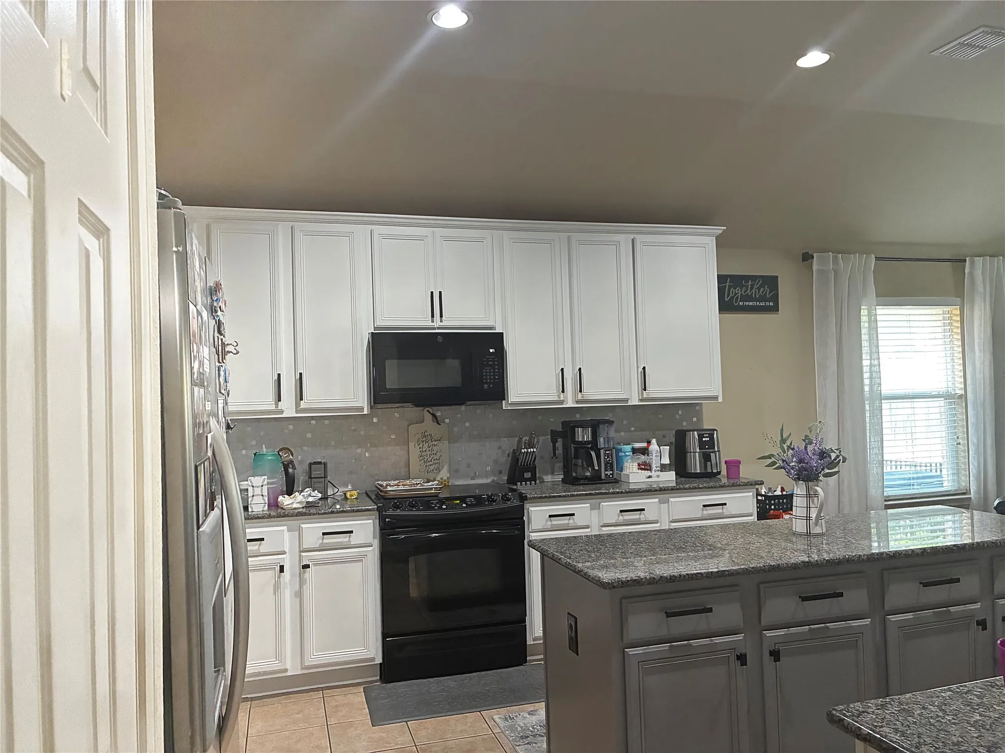 Kitchen featuring white cabinetry with dark hardware, a mosaic tile backsplash, black appliances, recessed lighting, and a kitchen island with a stone countertop