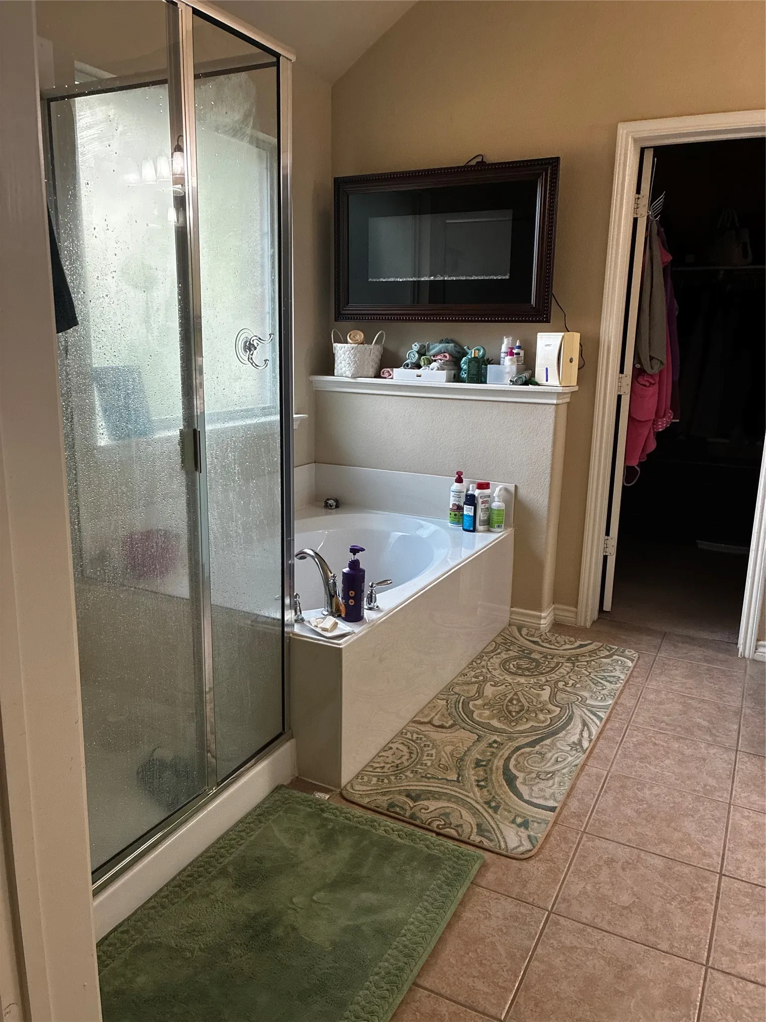 Bathroom featuring a glass-enclosed shower, a built-in soaking tub with a tiled surround, a mounted decorative accent, and neutral-toned tile flooring