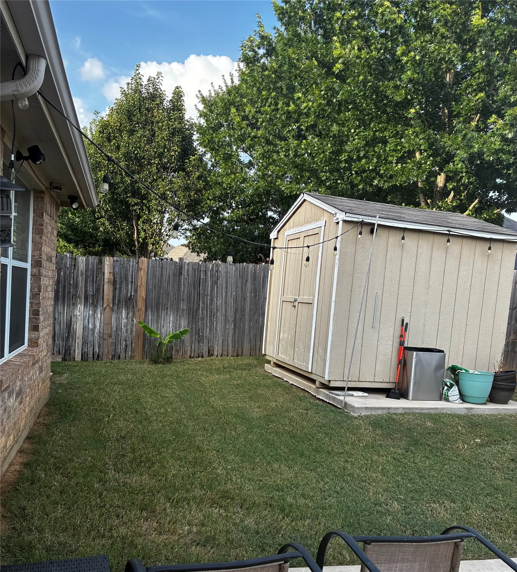 Expansive backyard featuring a manicured lawn, a detached storage shed with a shingle roof, a privacy fence, and mature trees providing natural shading