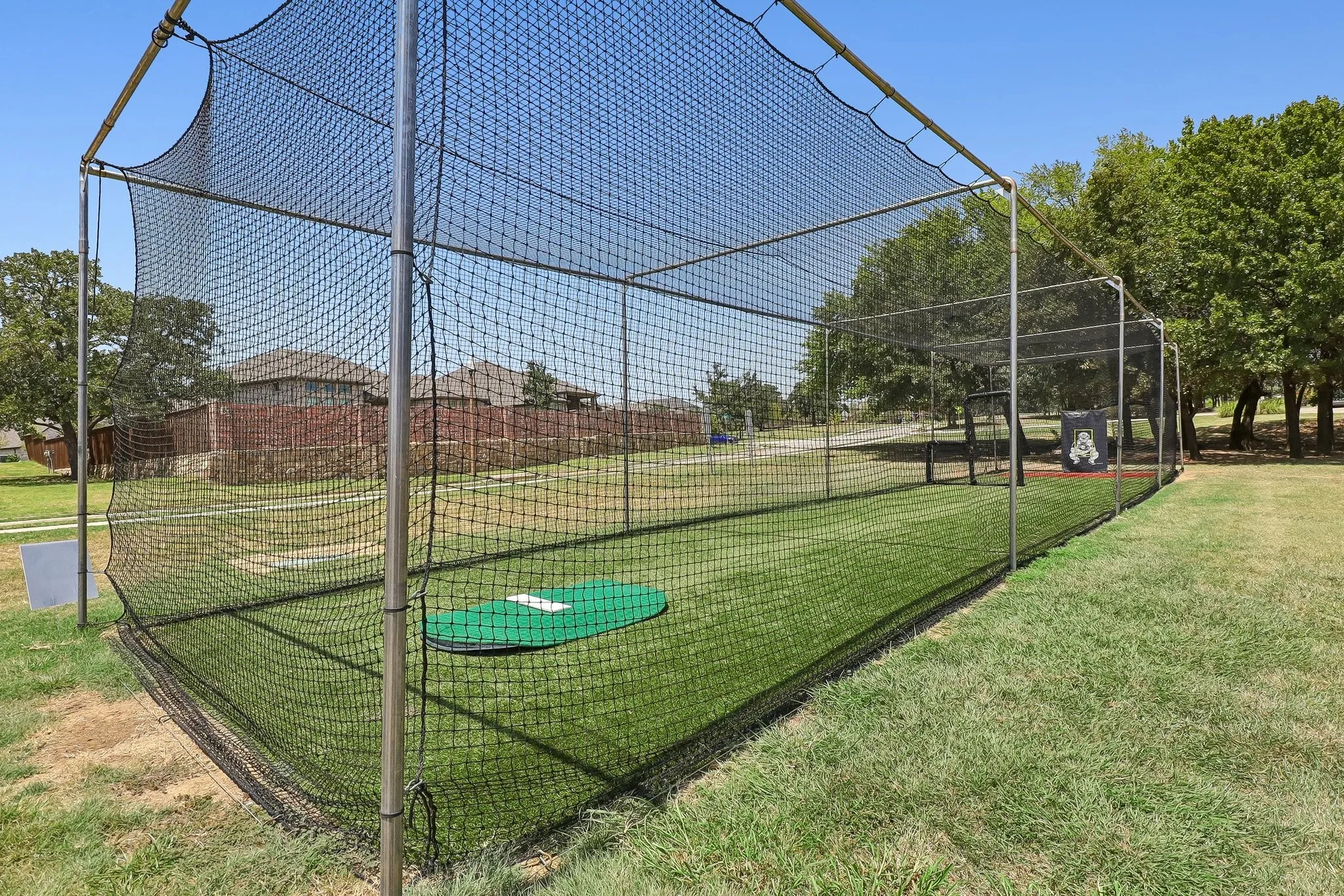 Outdoor batting cage with a full net enclosure, metal frame, artificial turf flooring, and a green home plate mat