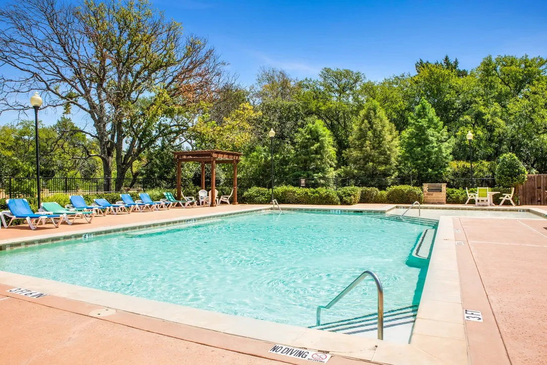 Rectangular swimming pool featuring a perimeter of concrete decking and a surrounding landscape of mature trees and shrubbery