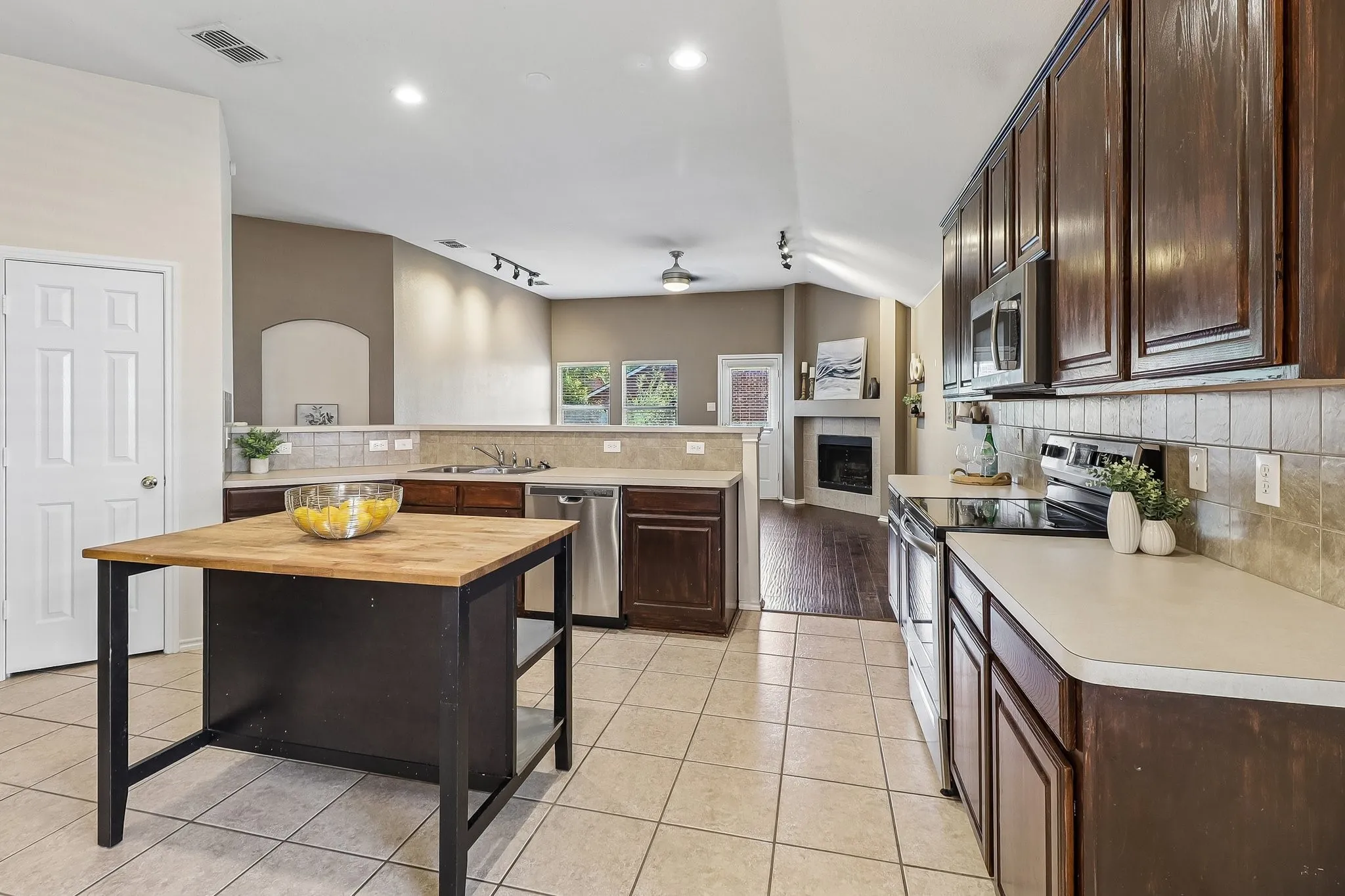 Spacious kitchen featuring dark wood cabinetry, stainless steel appliances, tile flooring, and a central island with a wood-finish countertop