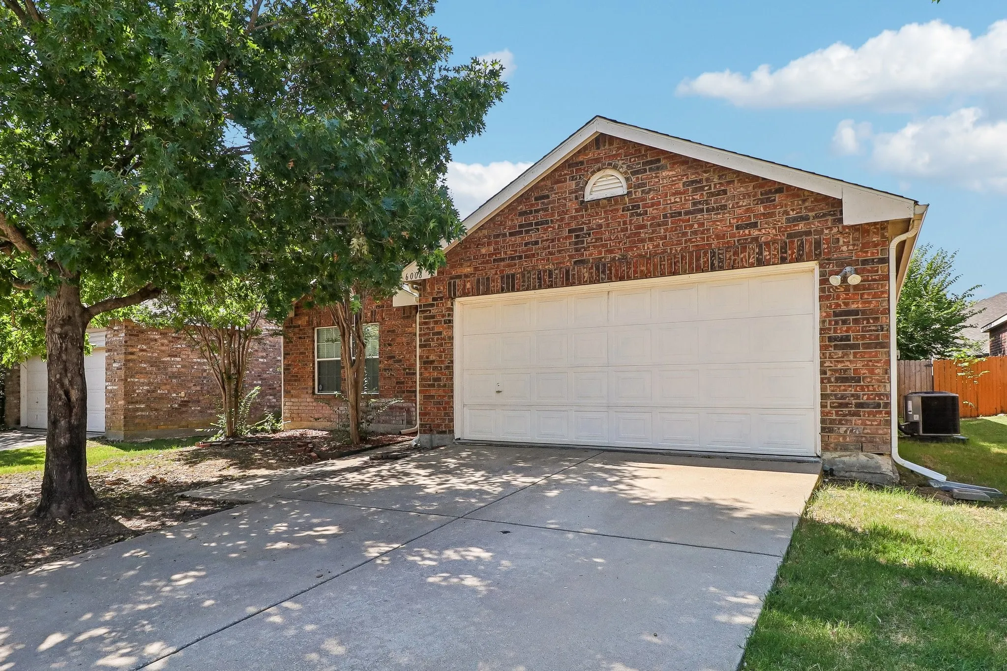 Brick facade residence featuring an attached garage with a concrete driveway, mature trees, and a manicured lawn