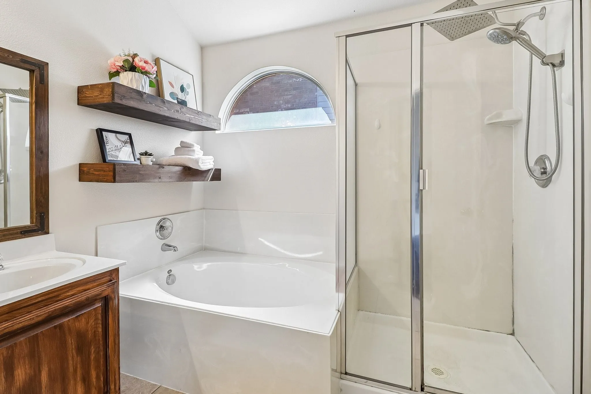 Bathroom featuring a corner soaking tub, a separate glass-enclosed shower with a rain shower head, and an arched window