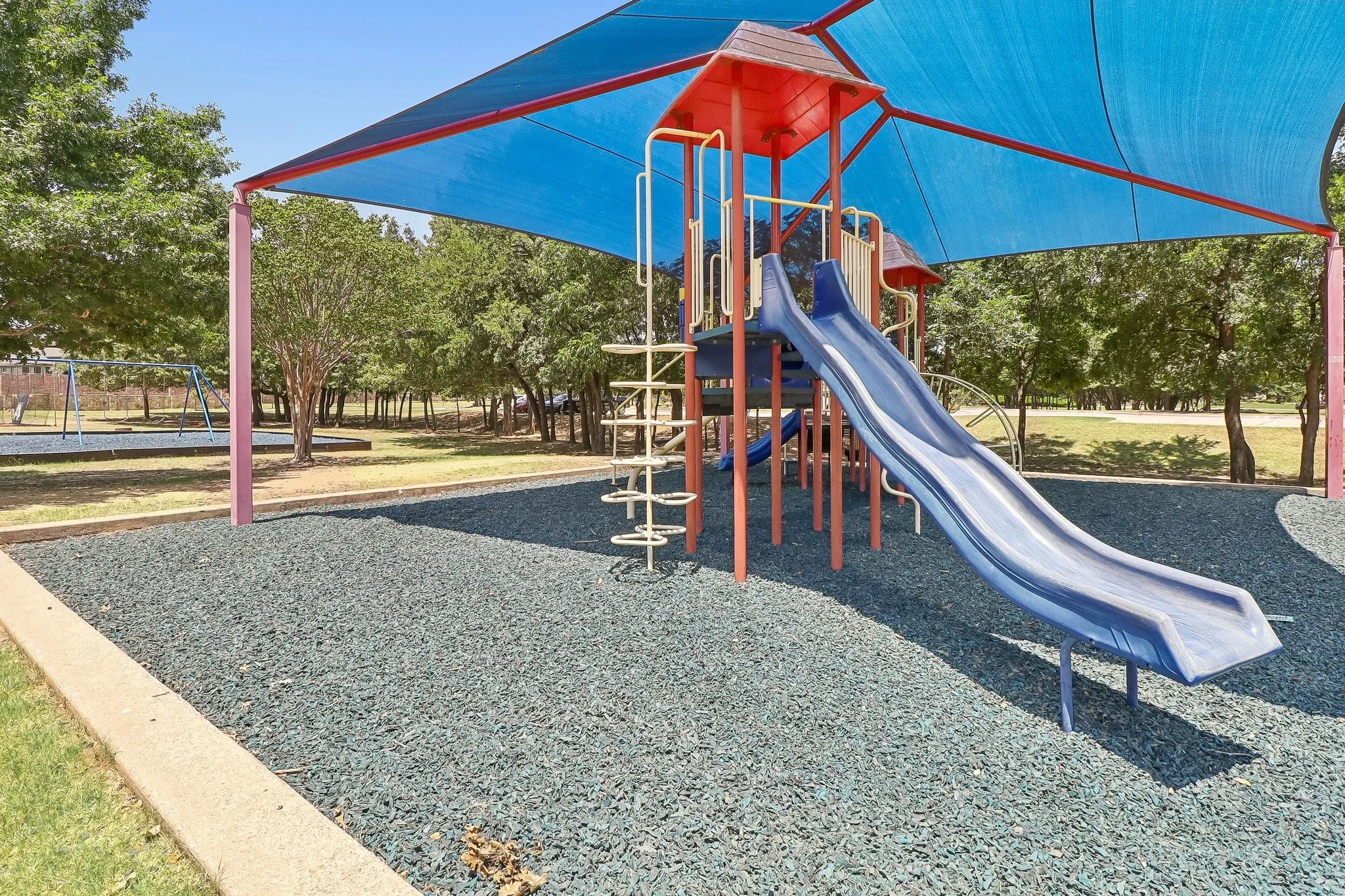 Recreational play structure featuring a blue slide, climbing elements, and a vibrant blue shade canopy