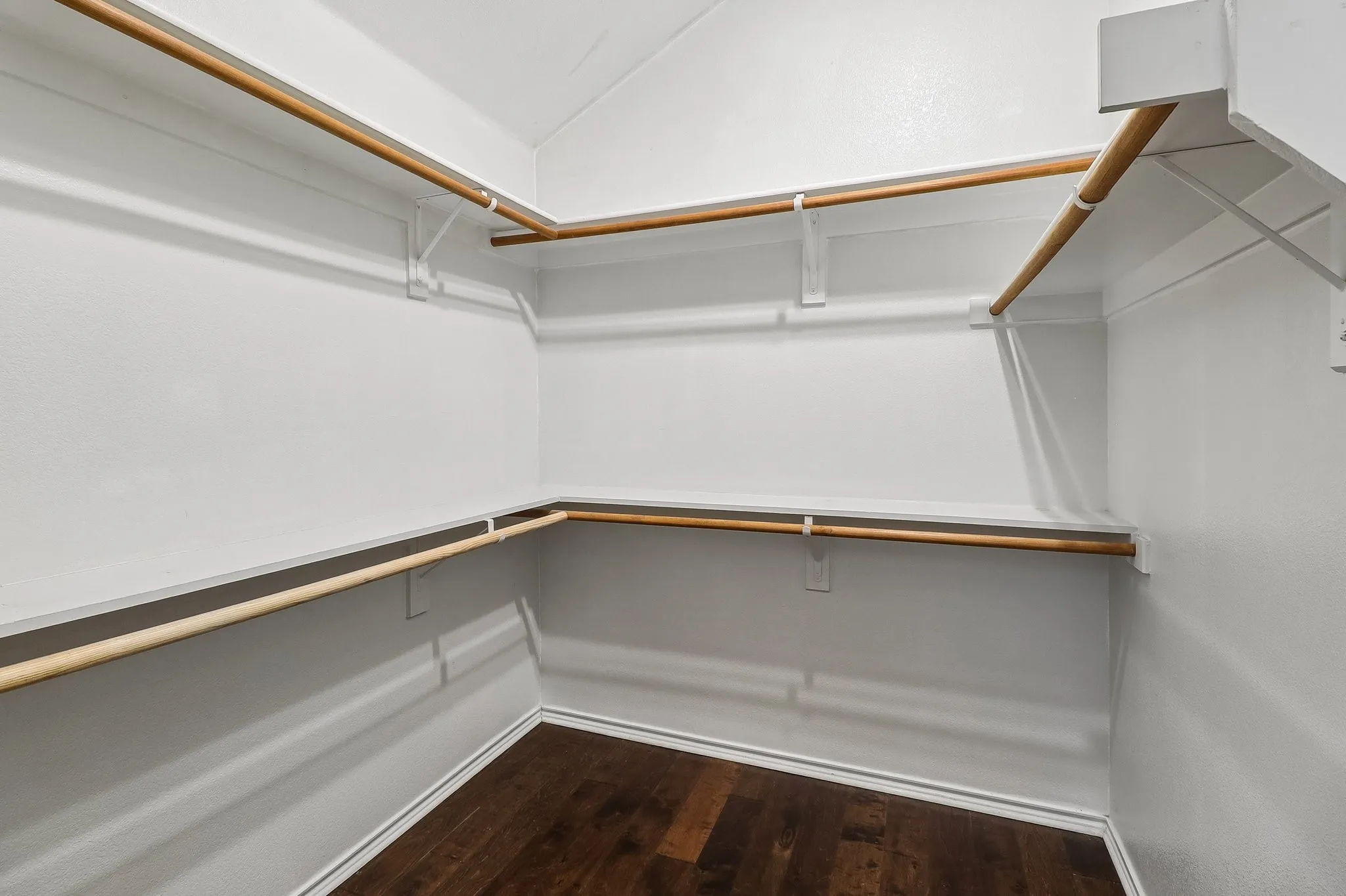 Spacious walk-in closet featuring wood-finish flooring, white walls, multiple shelving units, and ample hanging rods