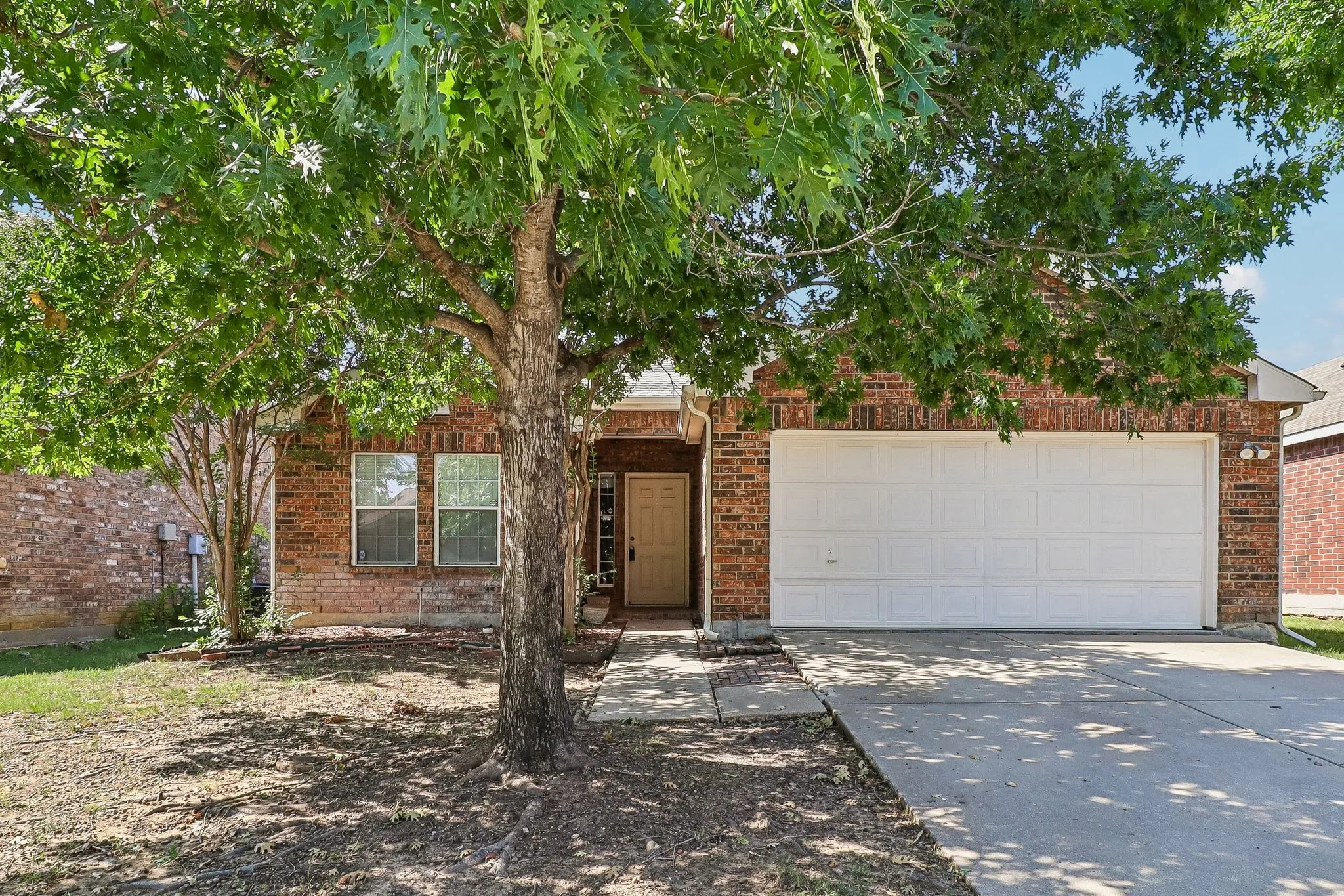 Brick exterior with an attached two-car garage, mature front yard trees, a concrete driveway, and a front entry door