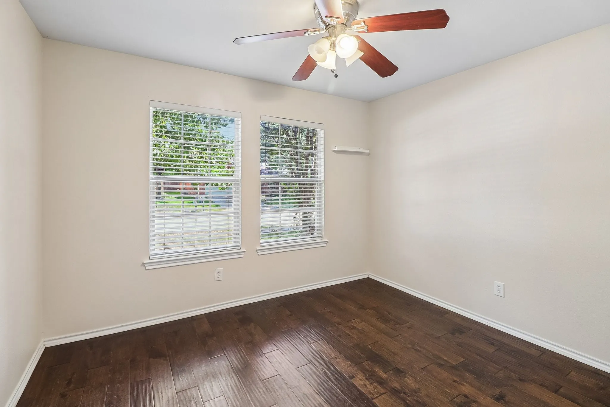 Room featuring two windows with horizontal blinds, wood-finish flooring, a ceiling fan with integrated lighting, and neutral wall tones