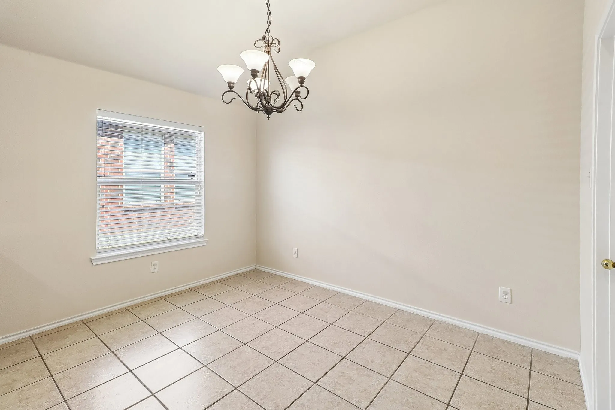 Open room featuring tile flooring, neutral wall paint, a single window with blinds, and a decorative ceiling light fixture