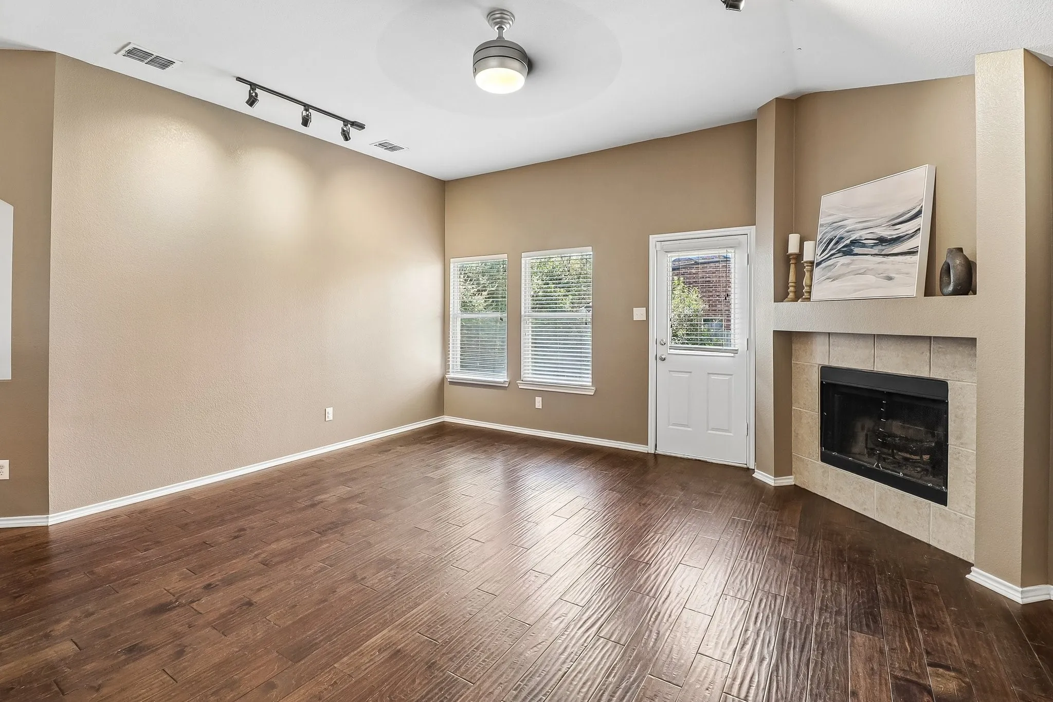 Living area featuring wood-finish flooring, a corner fireplace with a tiled surround, a built-in mantel, and multiple windows with blinds