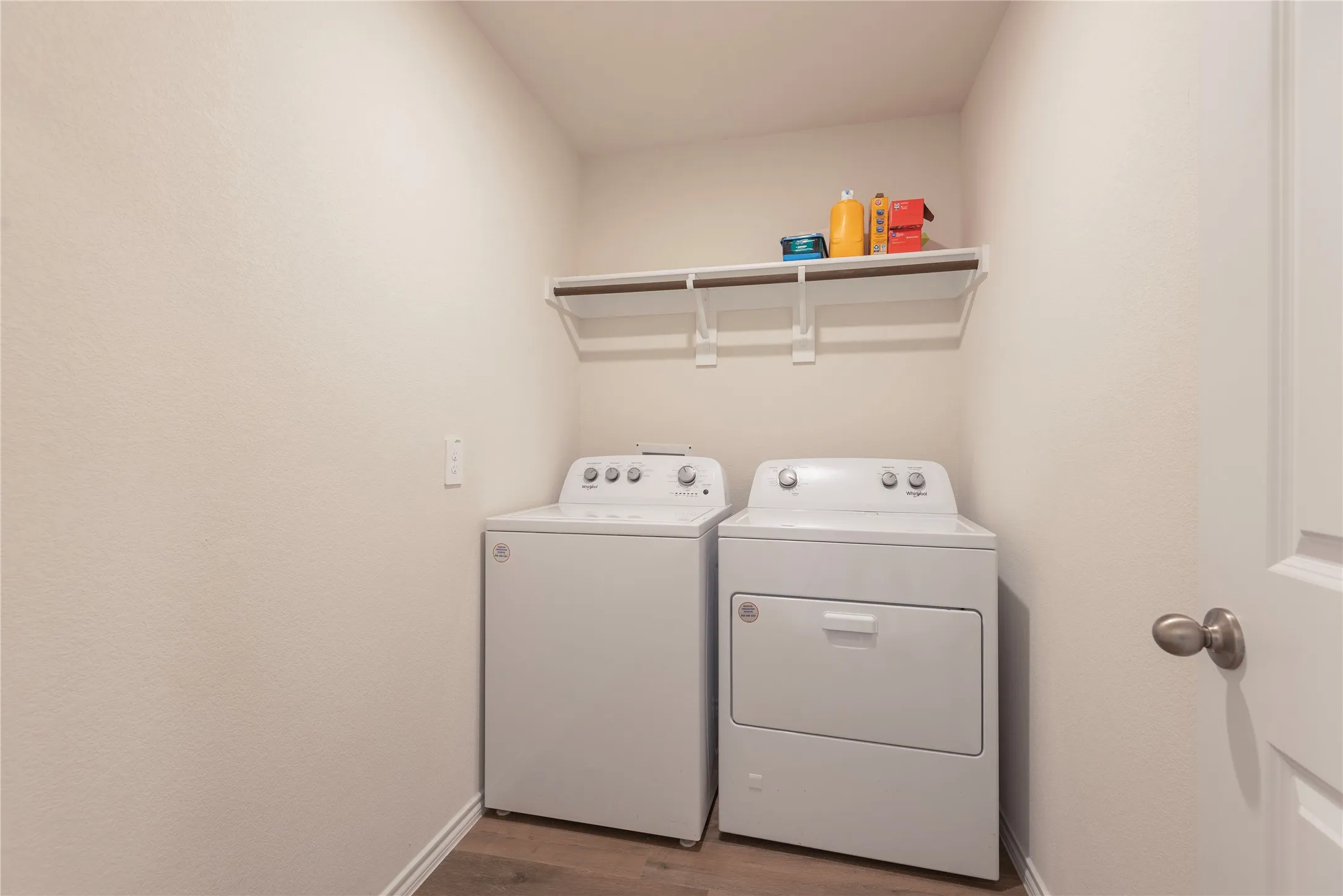 Dedicated utility area featuring wood-finish flooring, a wall-mounted shelving unit, and neutral wall tones