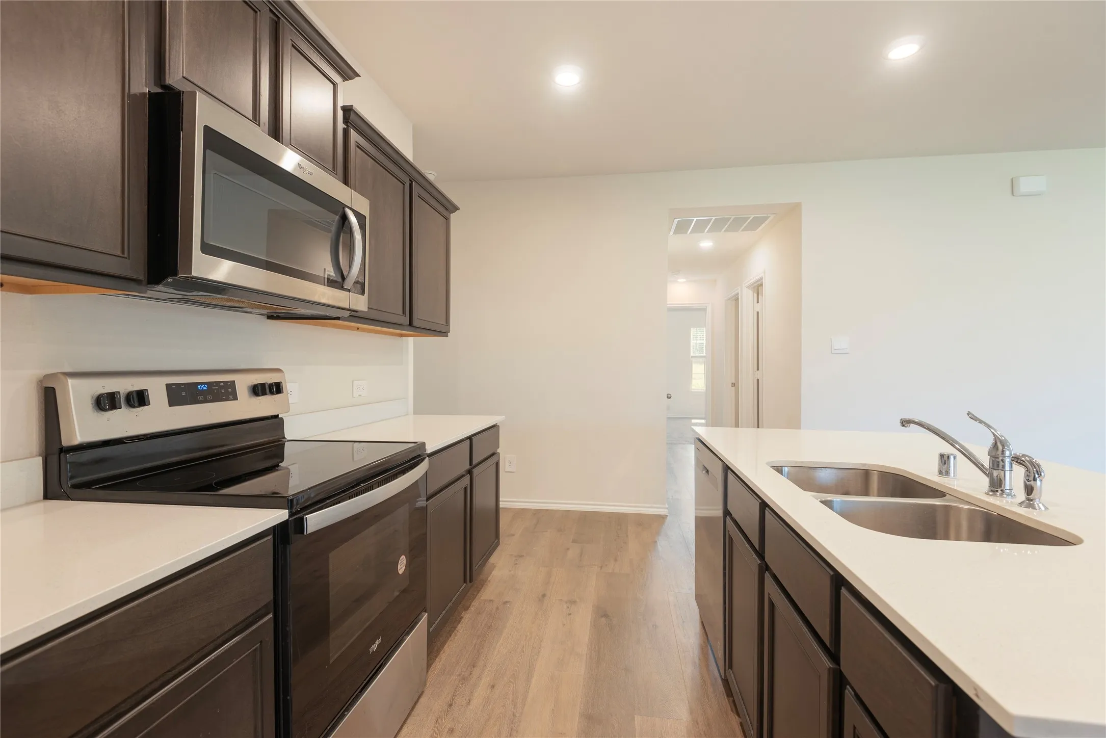 Contemporary kitchen featuring dark wood-finish cabinetry, light countertops, and stainless steel appliances