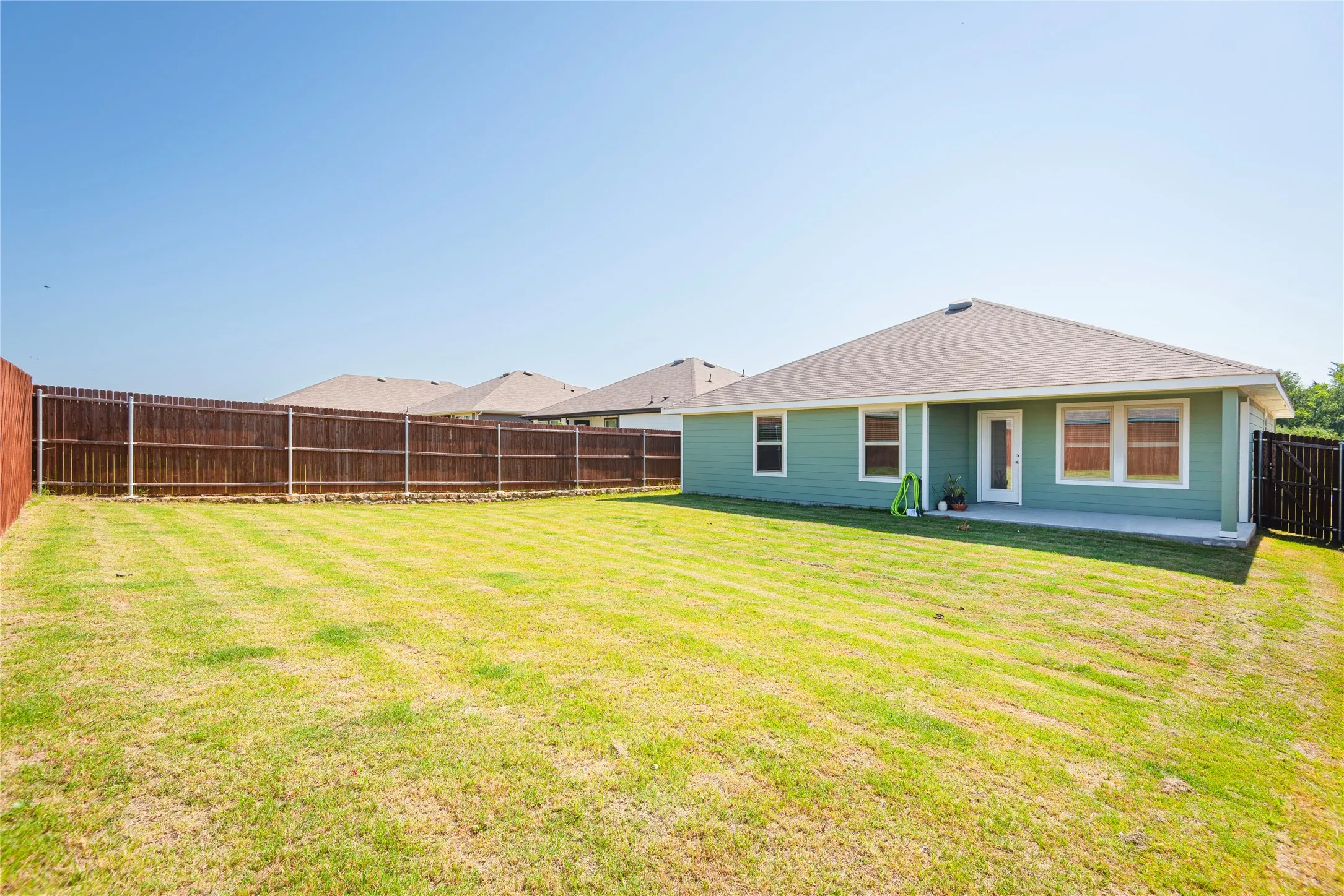 Expansive fenced backyard featuring a green lawn, a covered concrete patio, and a light green exterior