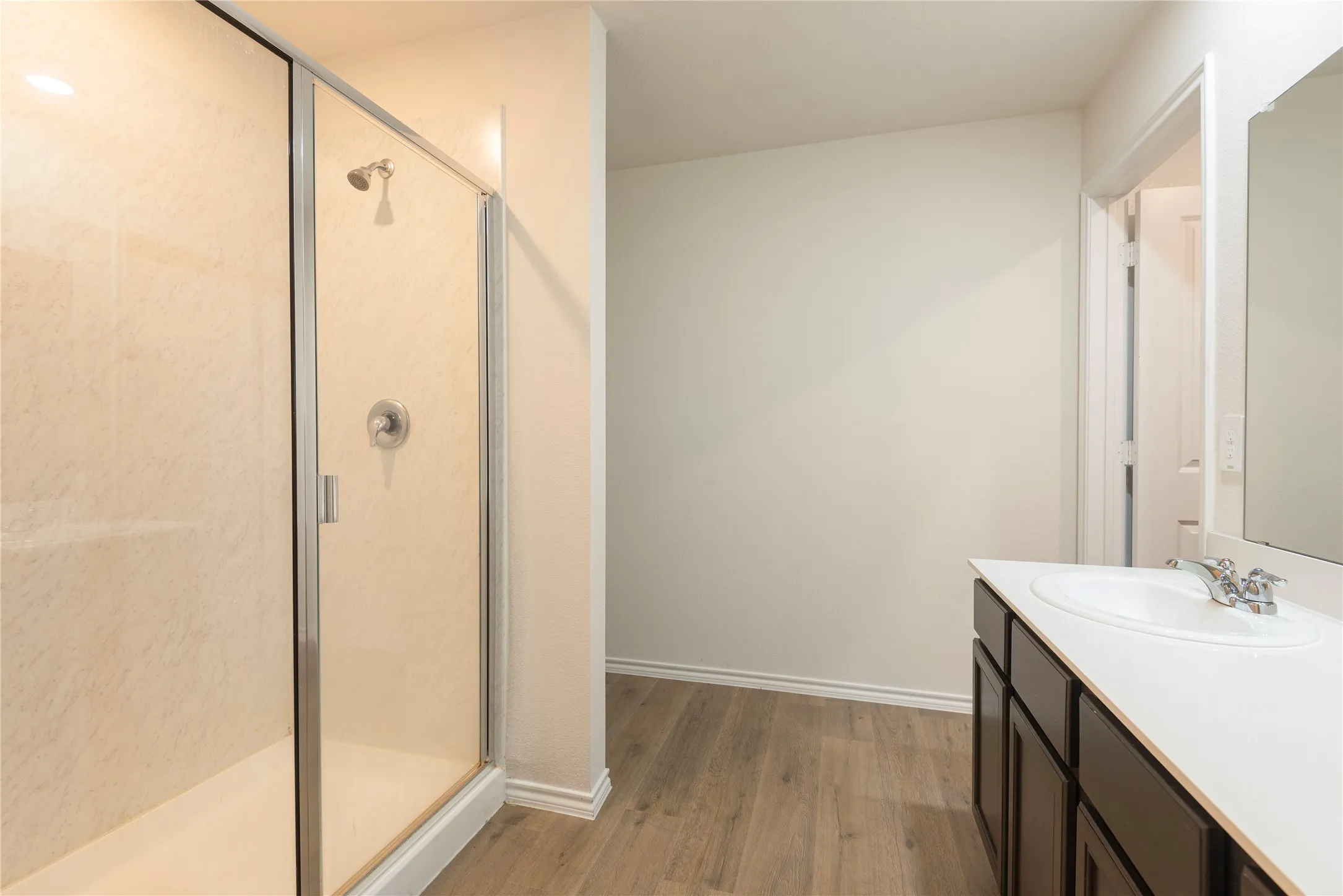 Glass-enclosed shower with light-toned wall panels and a chrome shower head