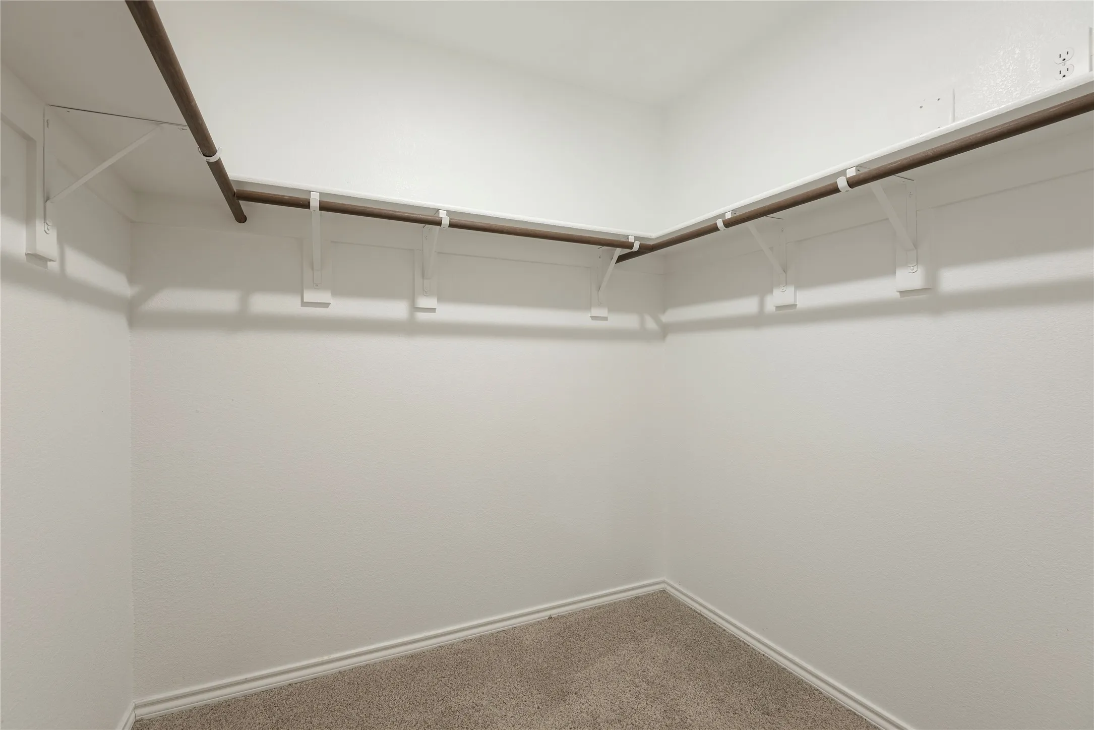 Primary Walk-in closet featuring light beige carpet, white baseboards, white textured walls, and a built-in shelving system with hanging rods