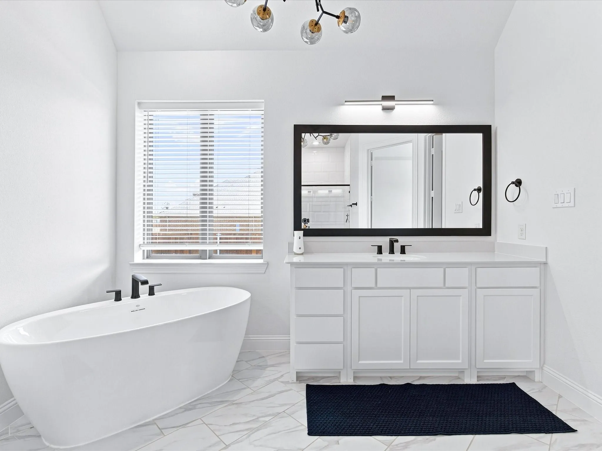 Freestanding soaking tub with matte black fixtures, white vanity with shaker-style cabinetry, quartz countertop, and large framed mirror