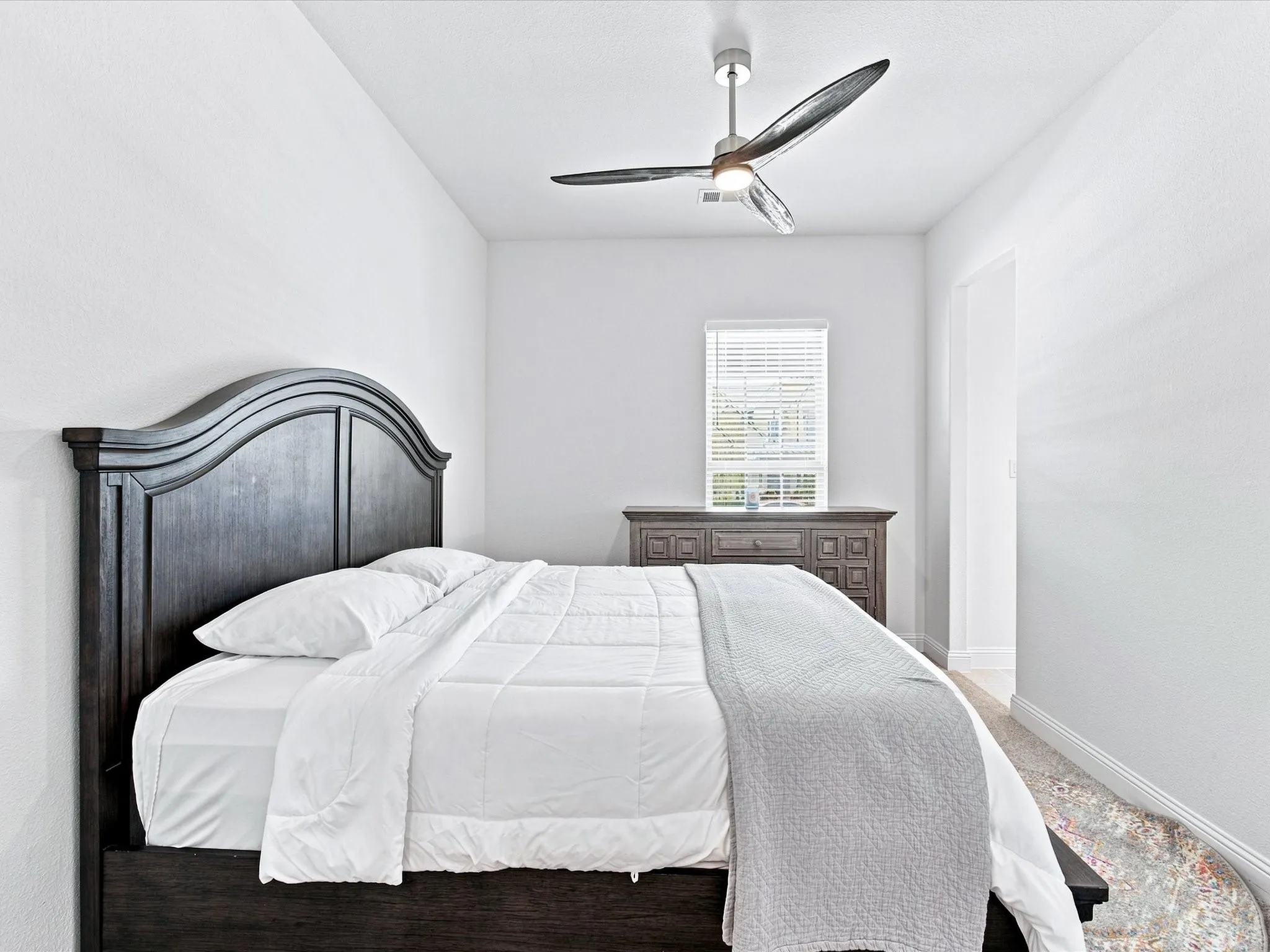 White interior walls, window with blinds, ceiling-mounted fan, and carpeted flooring