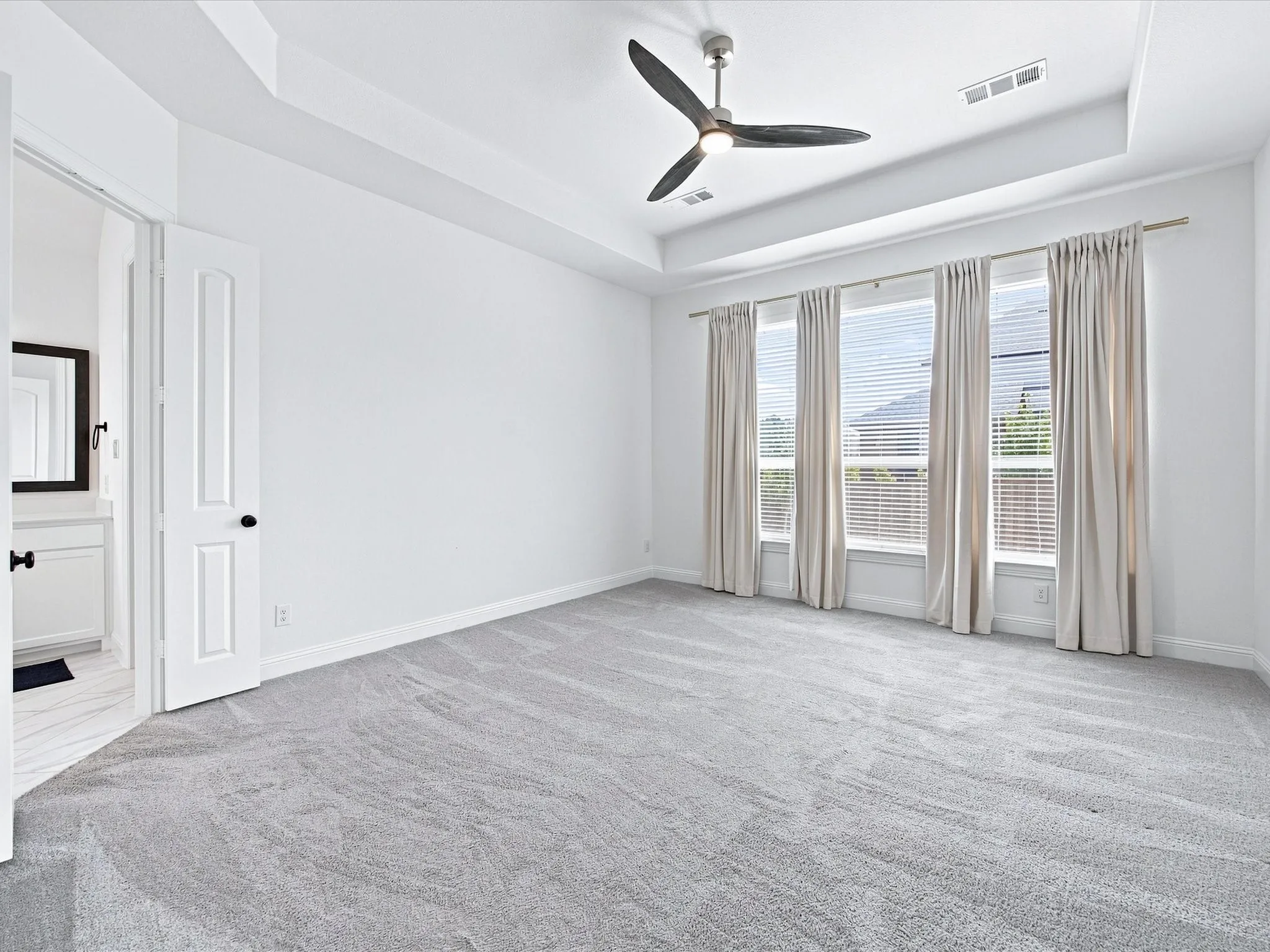 Recessed ceiling with a modern ceiling fan, light gray carpeting, and white paneled doors