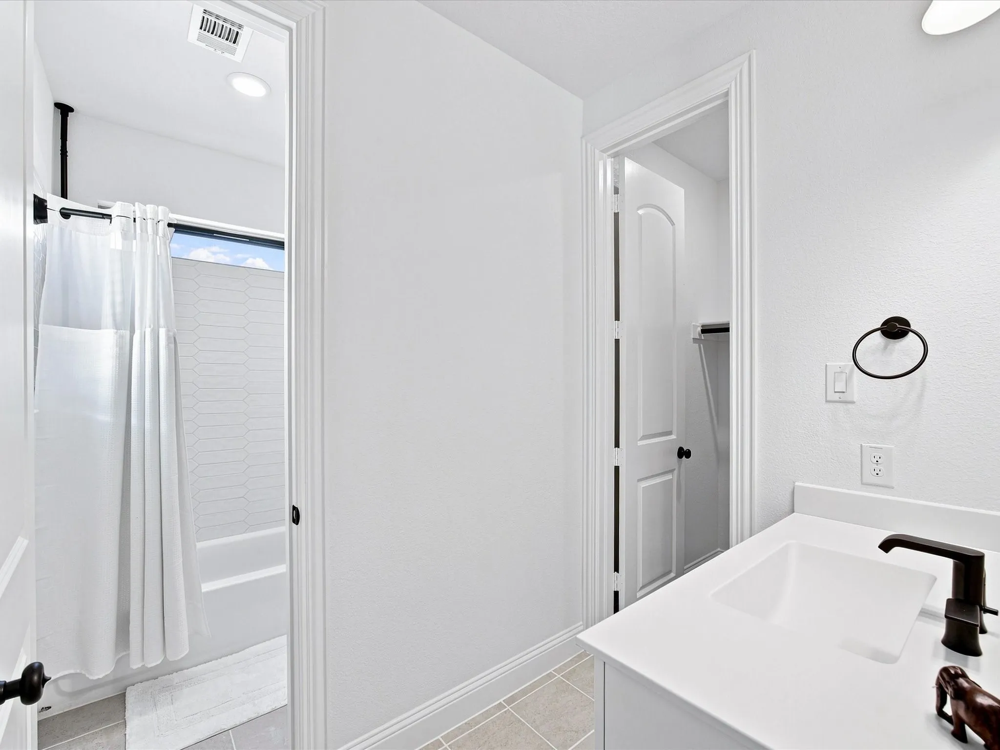 Bathroom featuring a white vanity with an integrated sink, dark bronze-finish fixtures, and light-toned floor tile