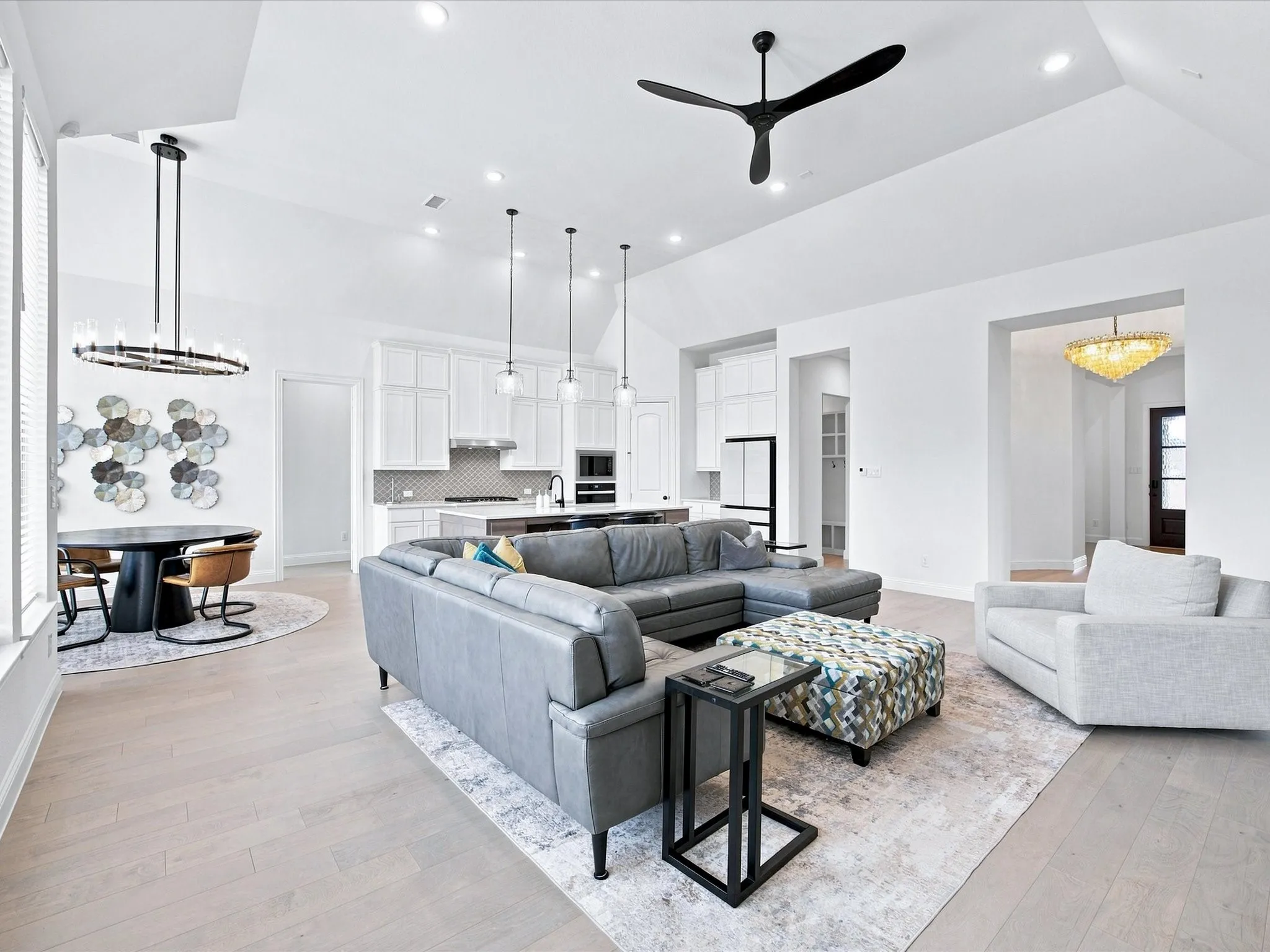 Vaulted ceilings, wood-finish flooring, recessed lighting, modern ceiling fan, and a contemporary chandelier
