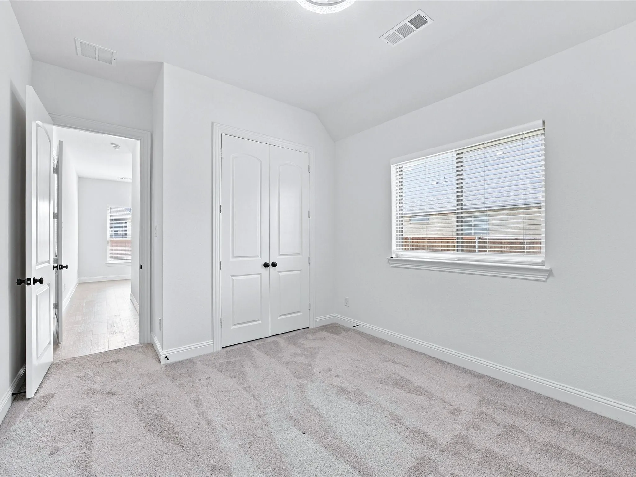 Plush carpeting, window with blinds, white trim throughout, white wall paint, and white double-door closet