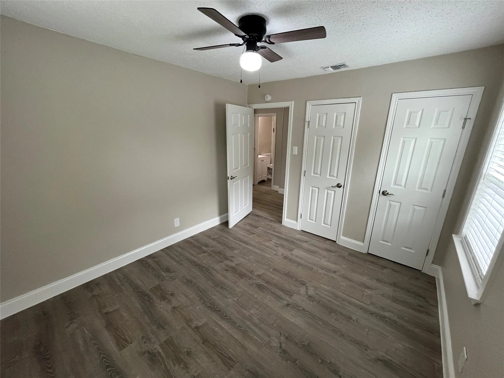 Room featuring wood-finish flooring, neutral wall tones, and a ceiling fan with light fixture