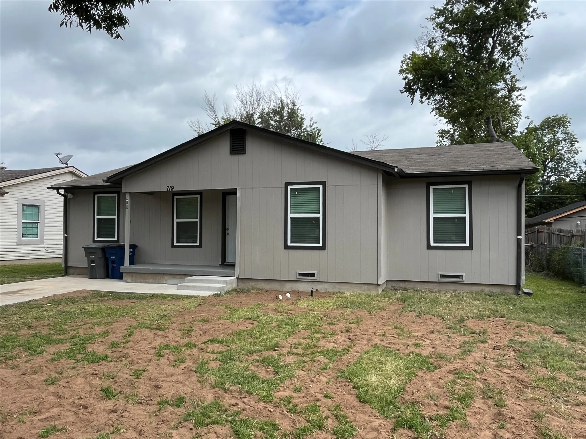 Single-story residence featuring light gray siding with dark trim, a covered front porch, and a concrete driveway