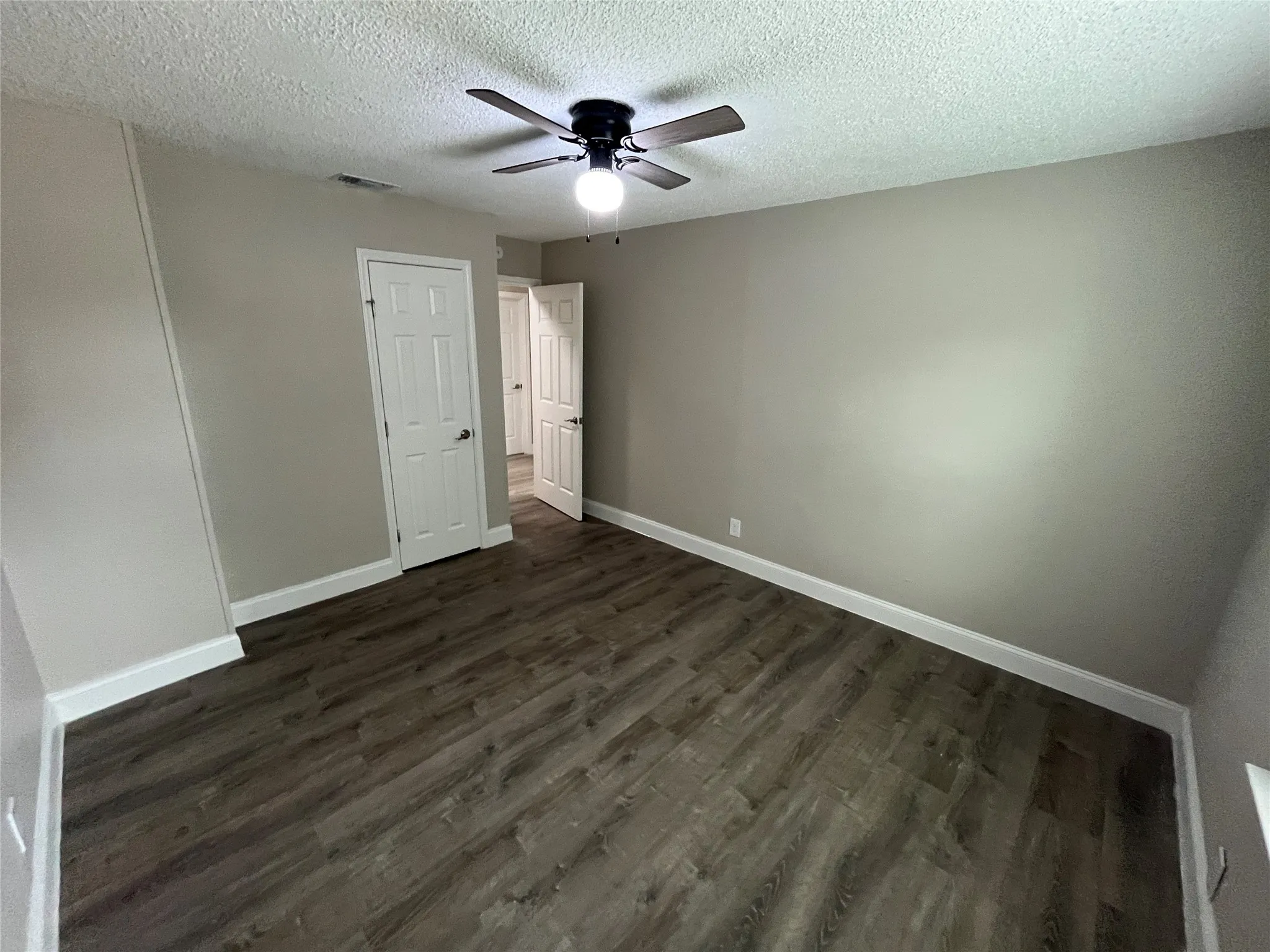 Spacious room featuring wood-finish flooring, neutral wall paint, white baseboards, and a ceiling fan with integrated lighting