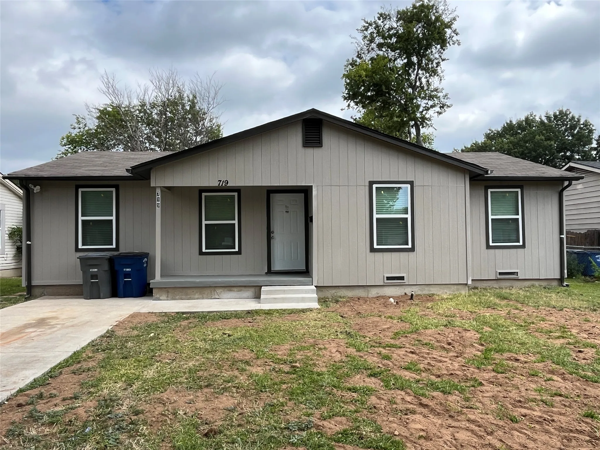 Single-story residence featuring light gray vertical panel siding with dark trim, a dark asphalt shingle roof, and a front concrete porch