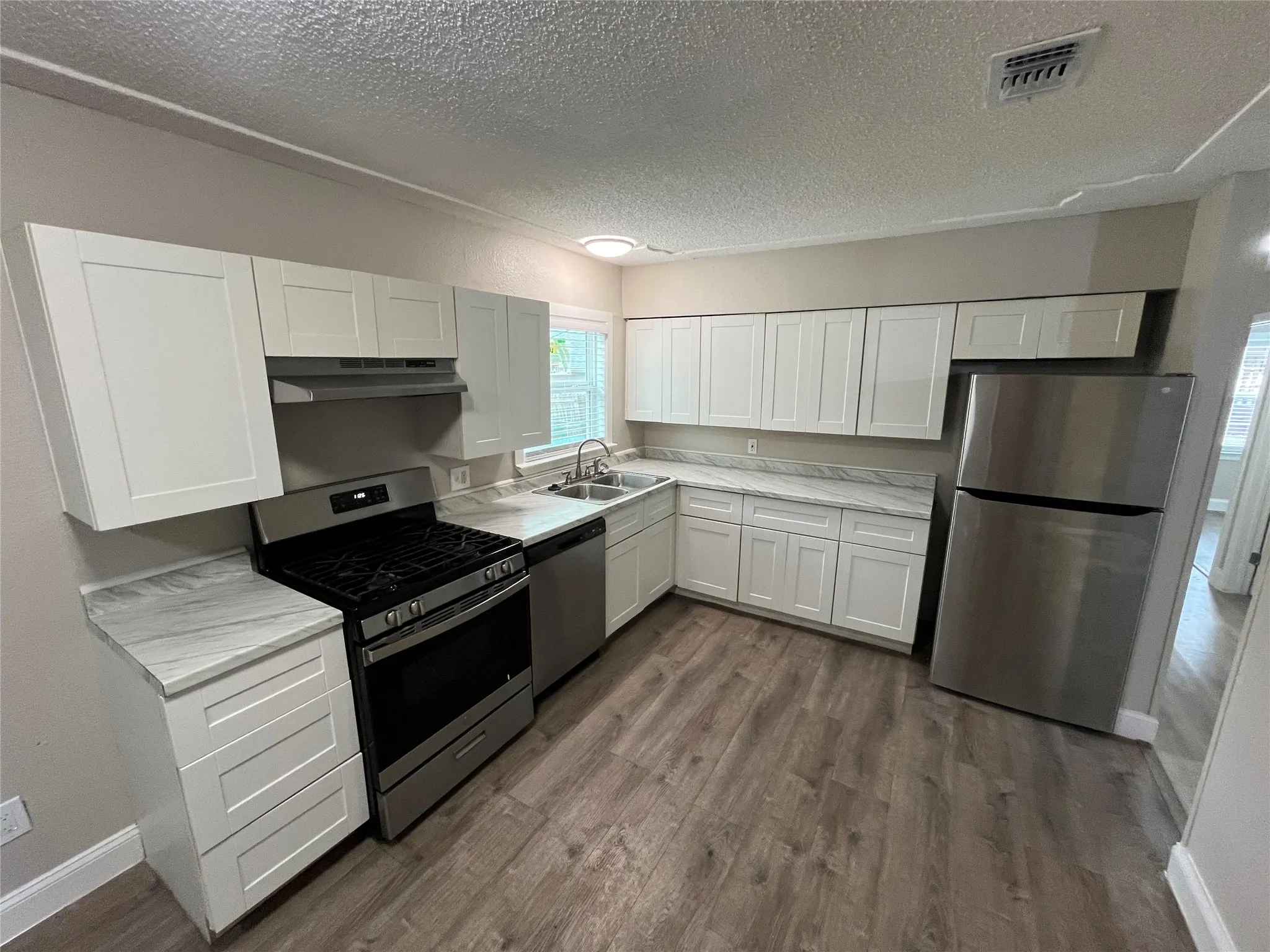 Modern kitchen featuring a gas range, stainless steel appliances, white shaker cabinetry, wood-finish flooring, and light-toned countertops