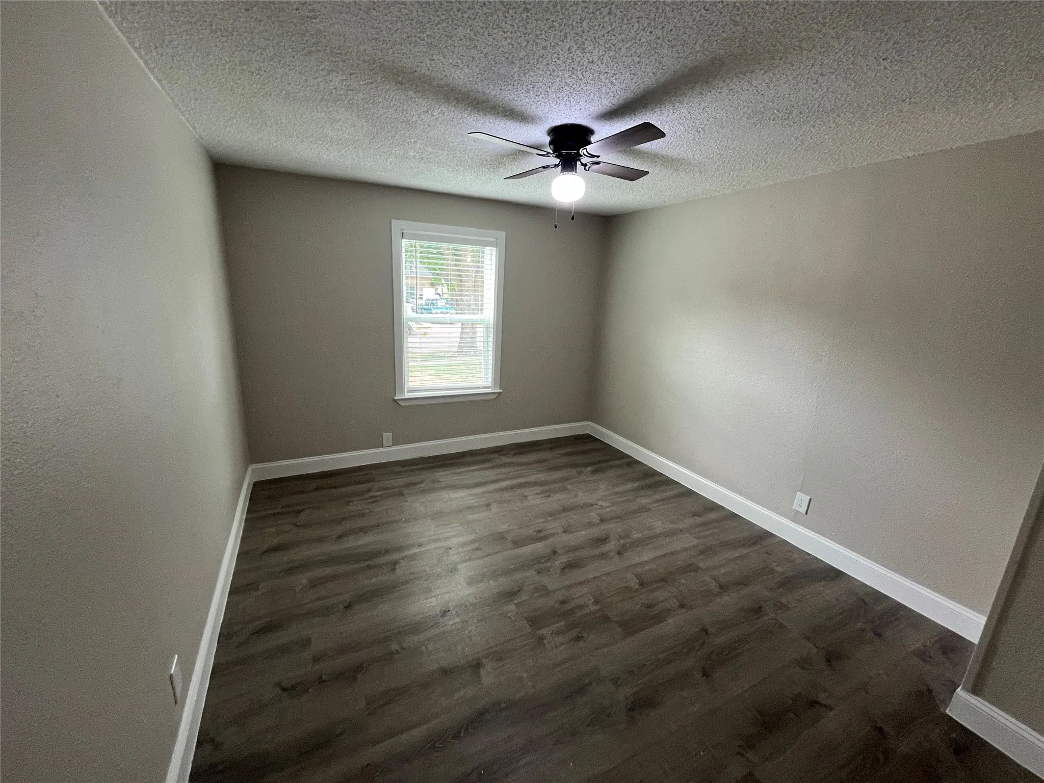 Bedroom featuring wood-finish flooring, neutral wall tones, a window with blinds, white baseboards, and a ceiling fan with integrated lighting