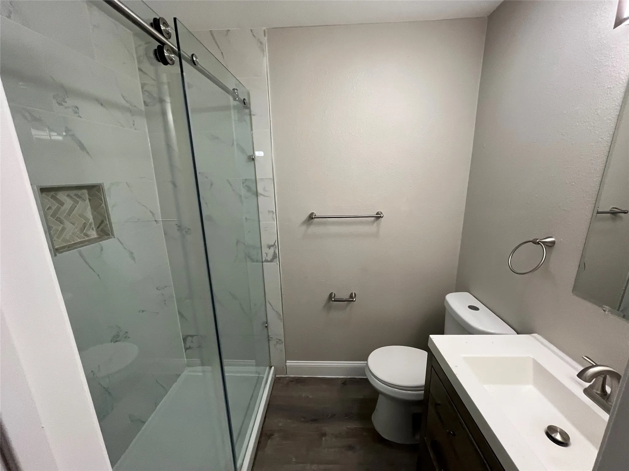 Contemporary bathroom featuring a spacious shower with sliding glass doors, white marble-look tile, and a recessed niche with herringbone pattern accent tile